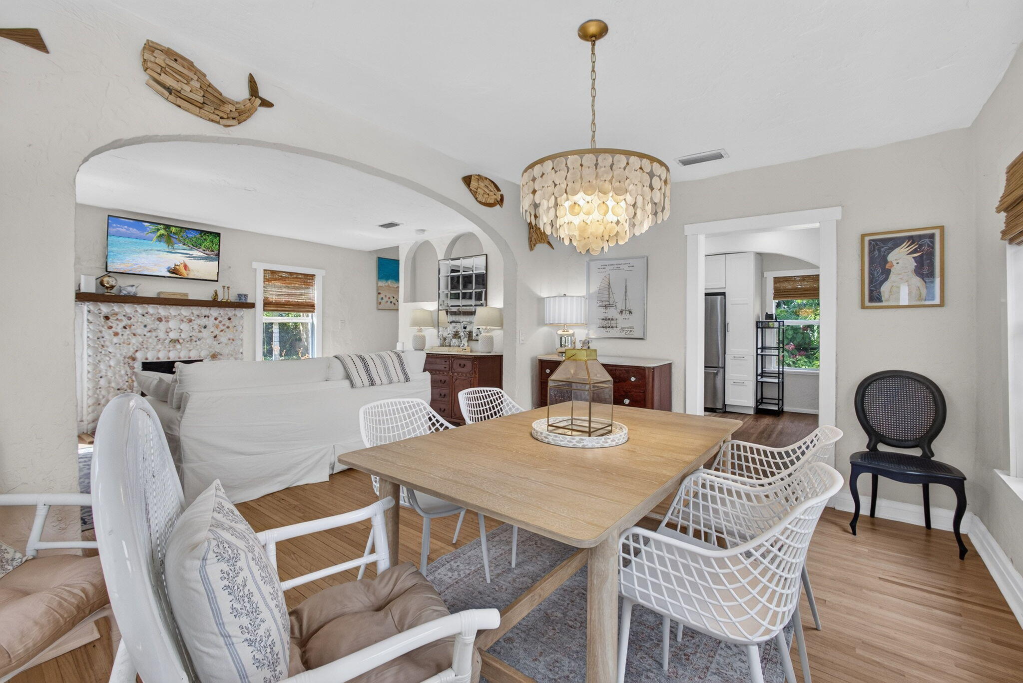 Dining area featuring wood-finish flooring, a tiered shell-detail chandelier, arched architectural entryways, and a fireplace with stone-textured surround