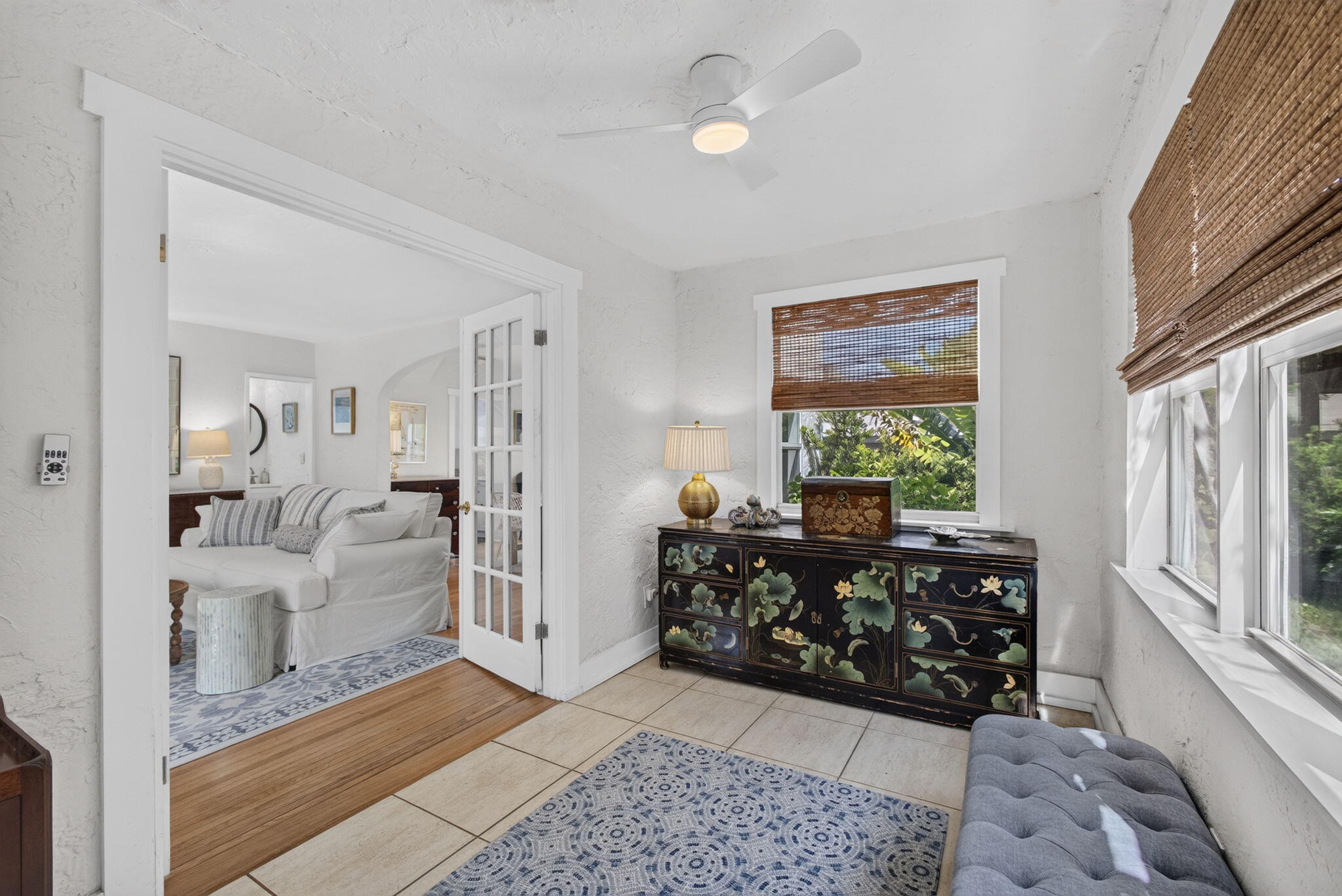 Textured wall finishes, large-format tile flooring, white-trimmed glass pane double doors, and a modern ceiling fan with integrated lighting