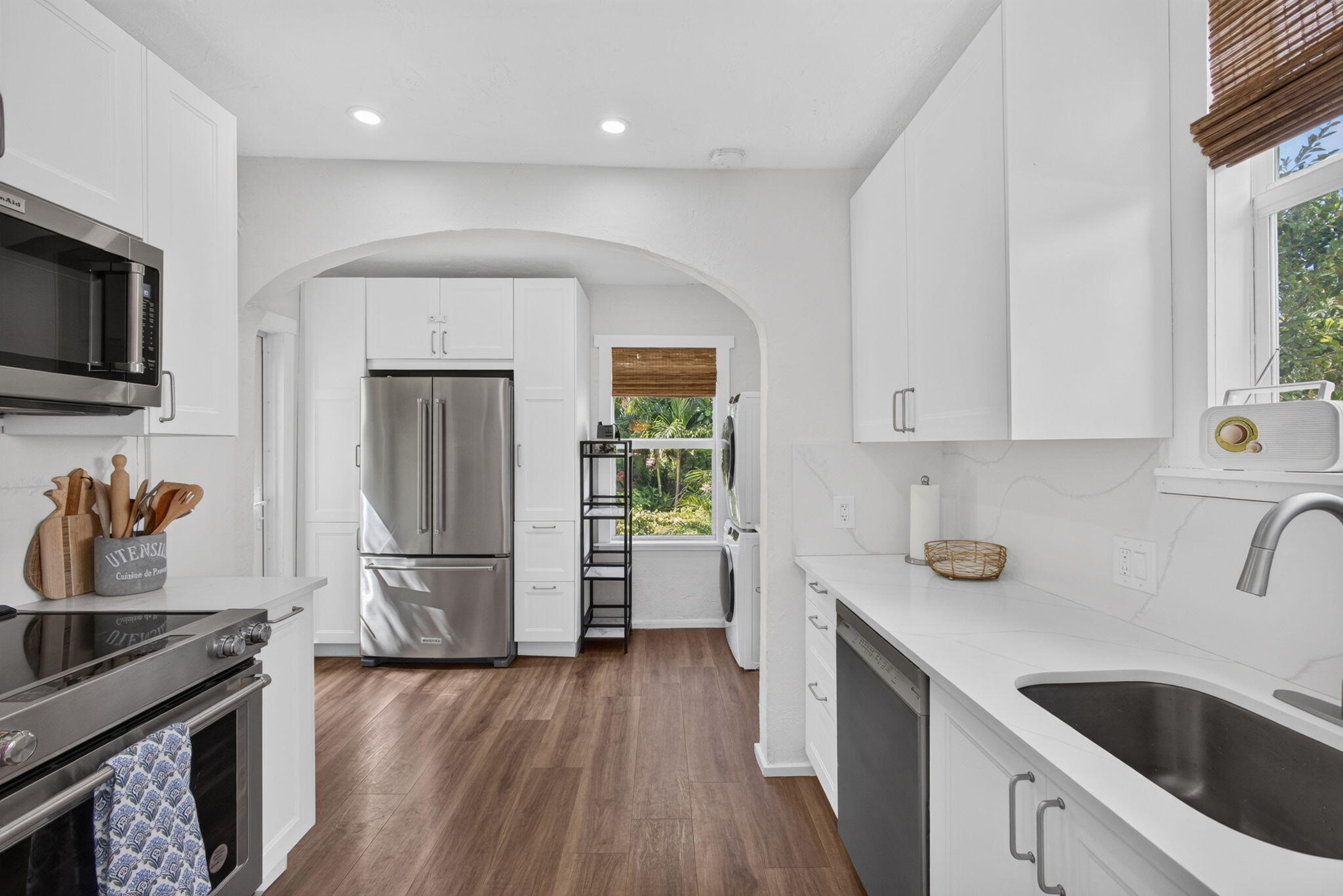 Kitchen featuring white shaker-style cabinetry, quartz countertops, stainless steel appliances, an arched doorway, and wood-finish flooring