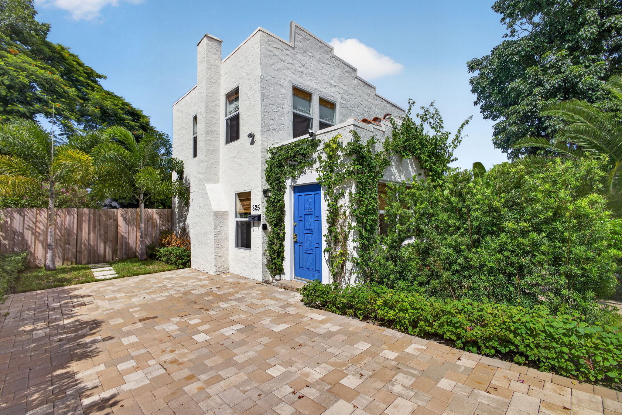 Stucco exterior featuring a parapet roofline, blue paneled front door, and paver driveway