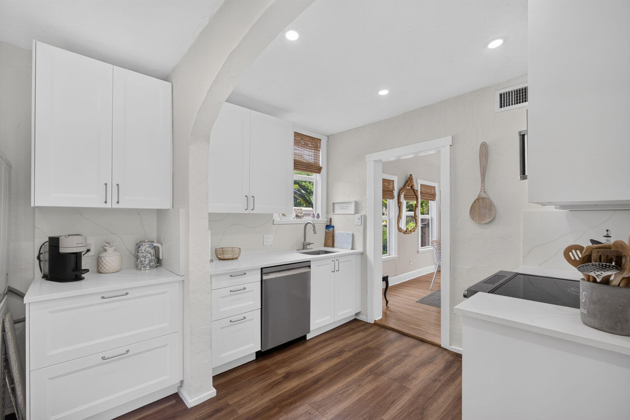 Kitchen featuring white shaker-style cabinetry, solid-surface countertops with stone-patterned backsplash, stainless steel dishwasher, wood-finish flooring, and recessed ceiling lighting