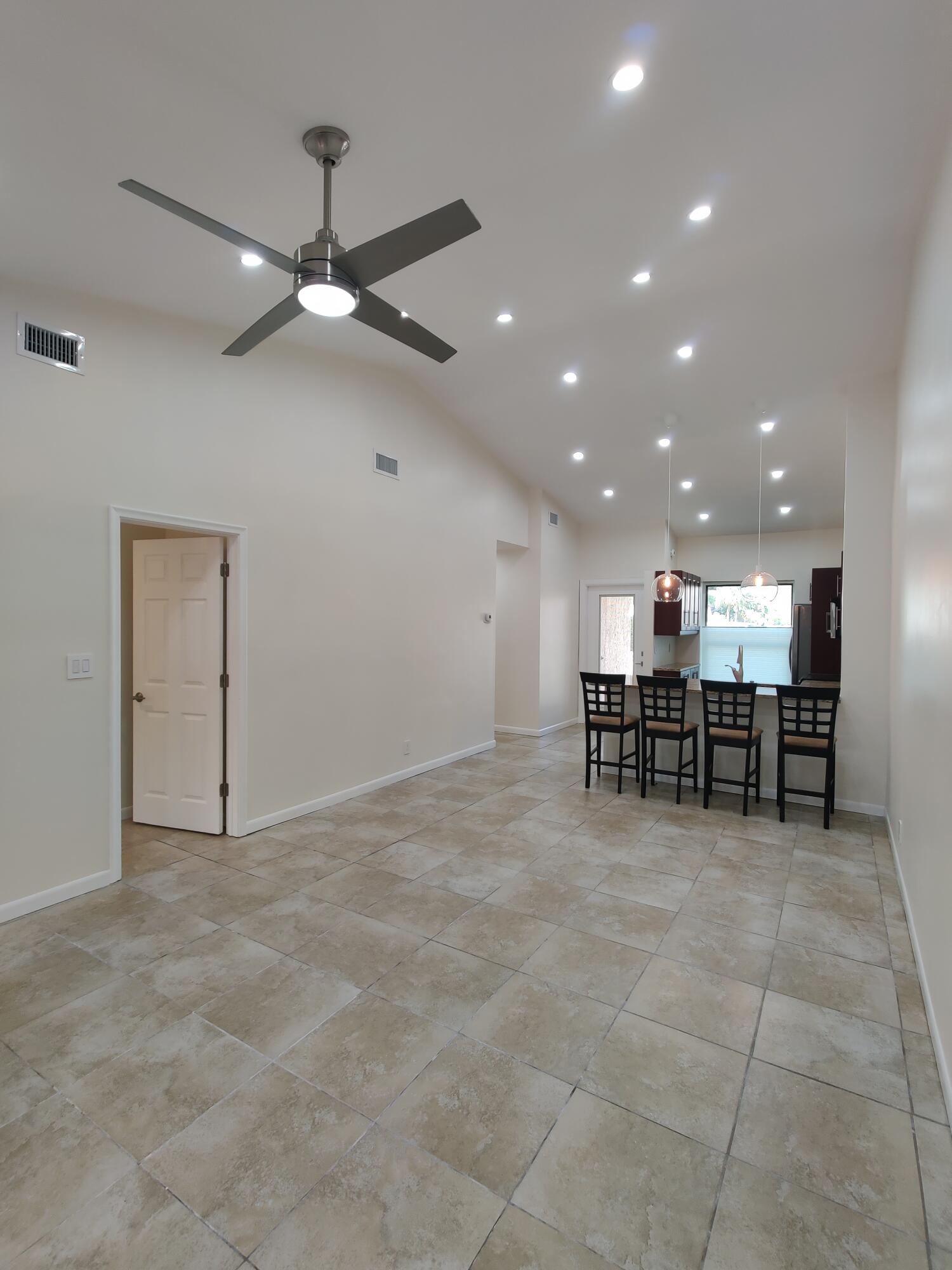 Vaulted ceilings featuring recessed lighting, a brushed-nickel ceiling fan, and large-format neutral tile flooring