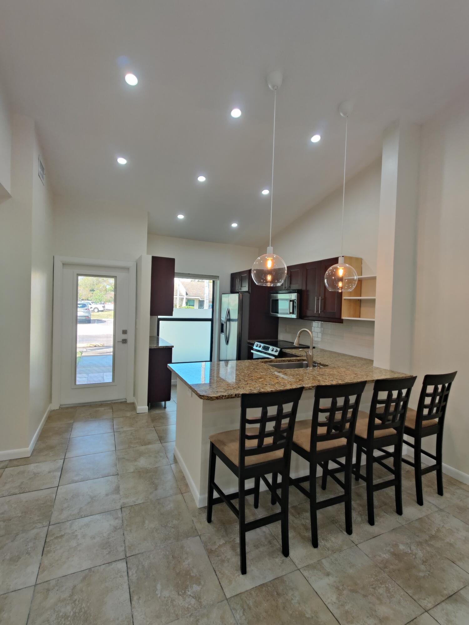 Kitchen featuring a stone-topped island, dark-toned cabinetry, recessed lighting, dual glass pendant lights, and tile flooring