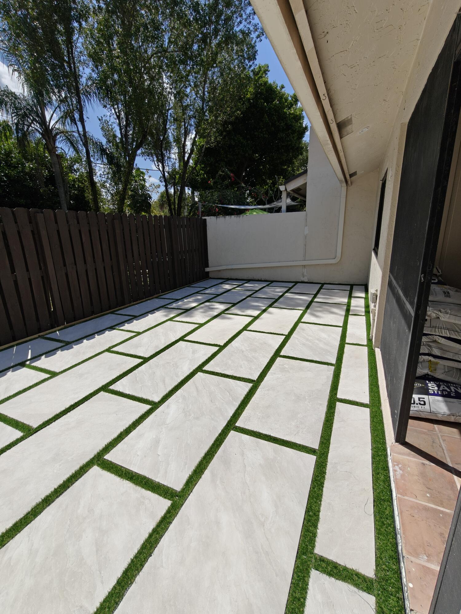 Paver patio featuring large-format concrete tiles with synthetic turf ribbon accents and a privacy wood fence