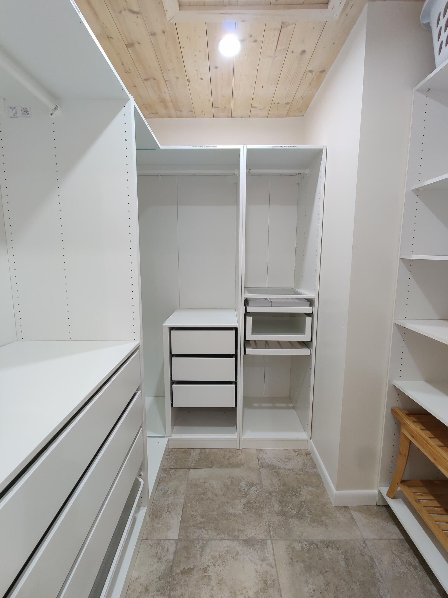 Walk-in closet featuring custom white cabinetry with integrated drawer storage, open shelving, tile flooring, and a natural wood-plank ceiling