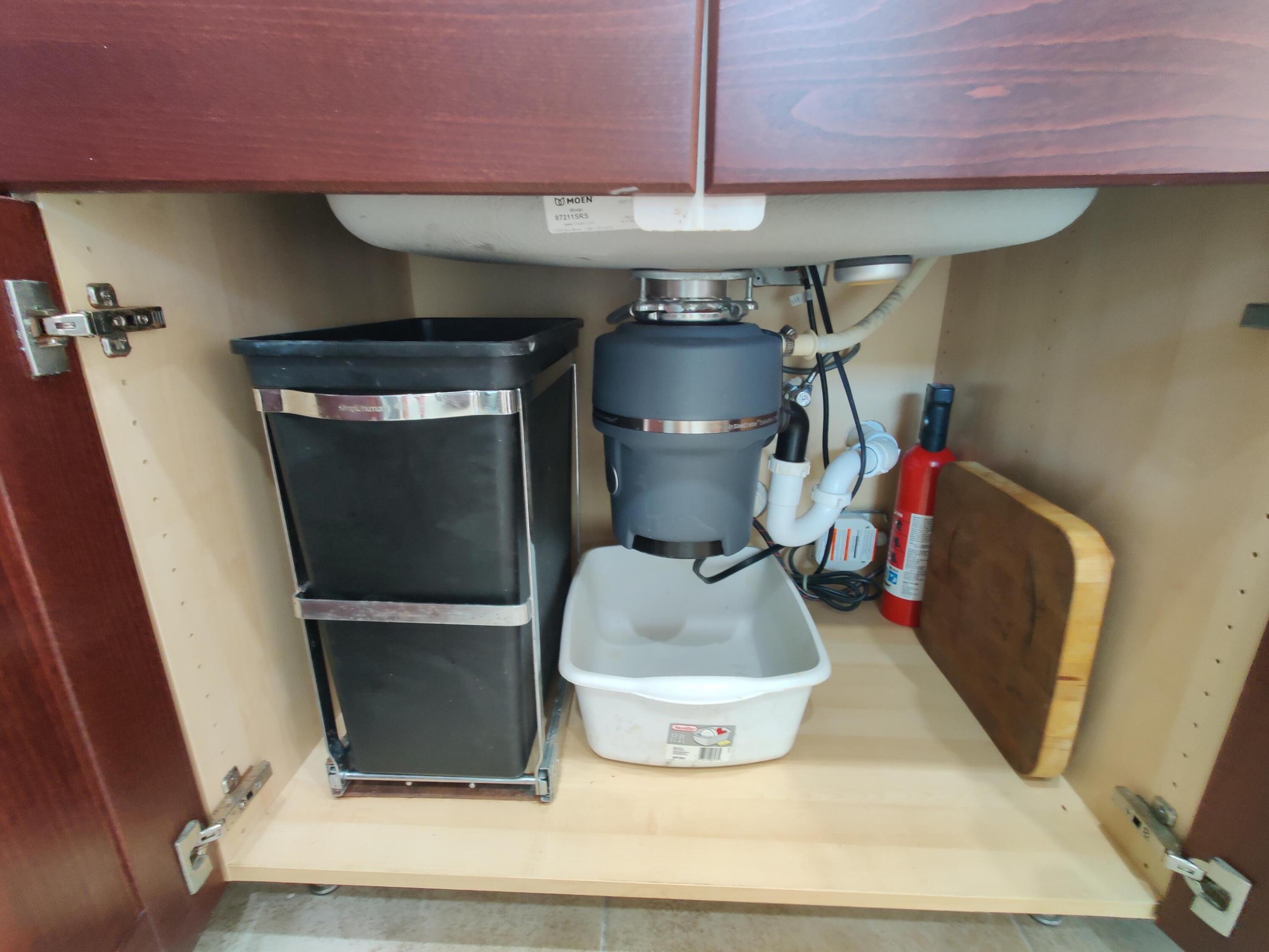Undermount sink plumbing featuring a garbage disposal unit and a built-in pull-out waste container system housed within wood-finish cabinetry