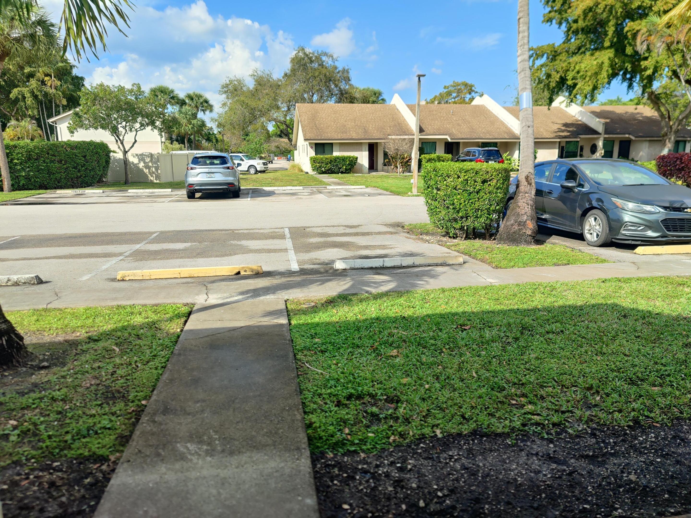 Asphalt parking area featuring designated spaces with concrete wheel stops, manicured lawn, and concrete walkways