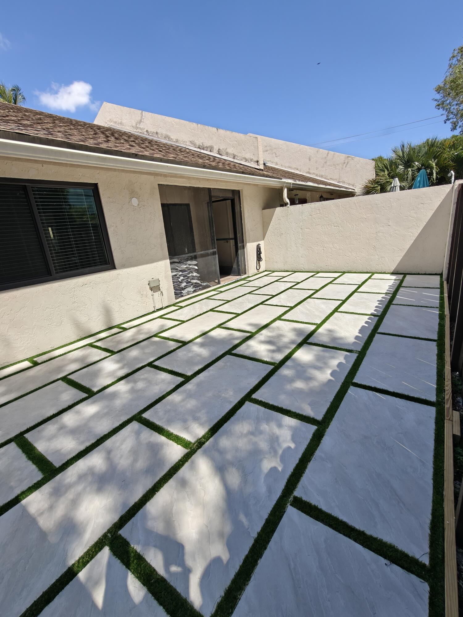 Outdoor patio featuring large-format concrete pavers with artificial turf inlay and a solid perimeter privacy wall