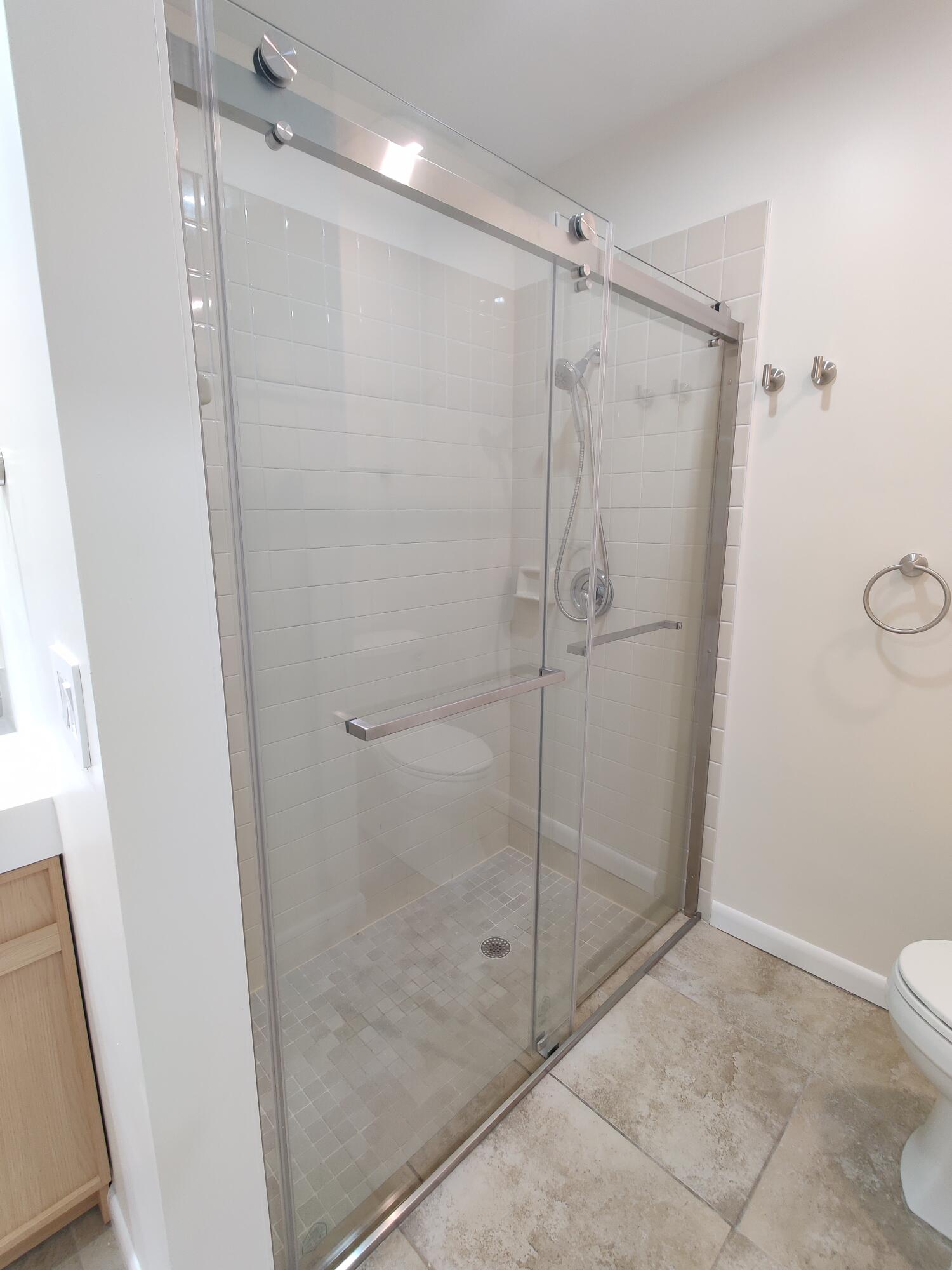Walk-in shower featuring a frameless sliding glass door, brushed nickel hardware, handheld shower fixture, and subway tile surround