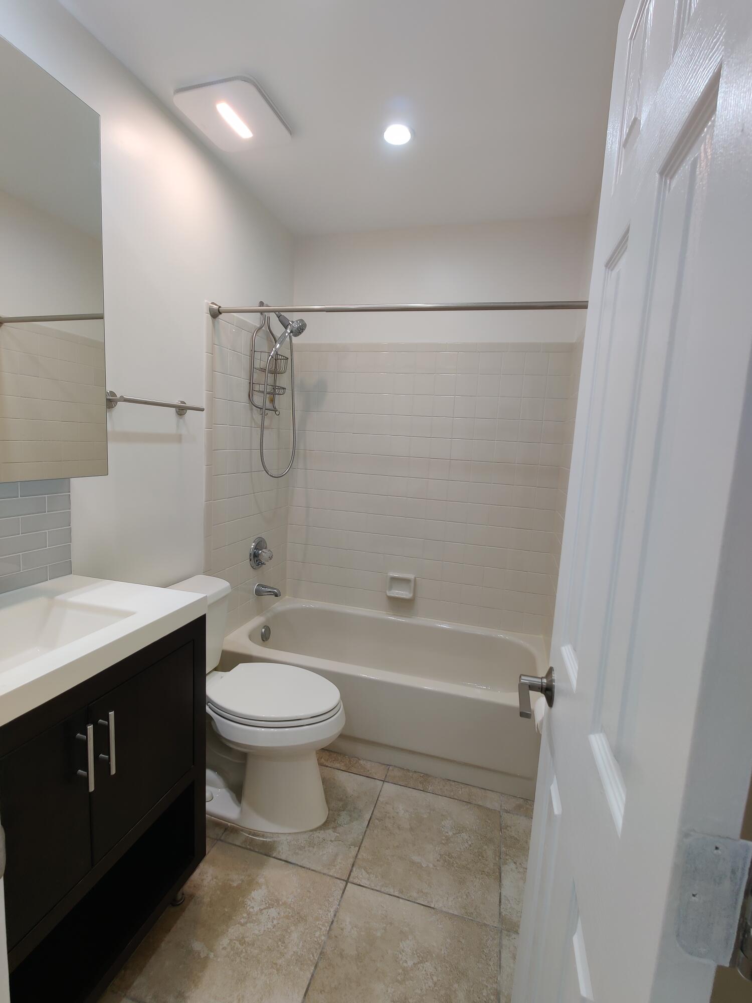 Bathroom featuring a dark wood-finish vanity with a white countertop, subway tile shower surround, integrated bathtub, and tile flooring