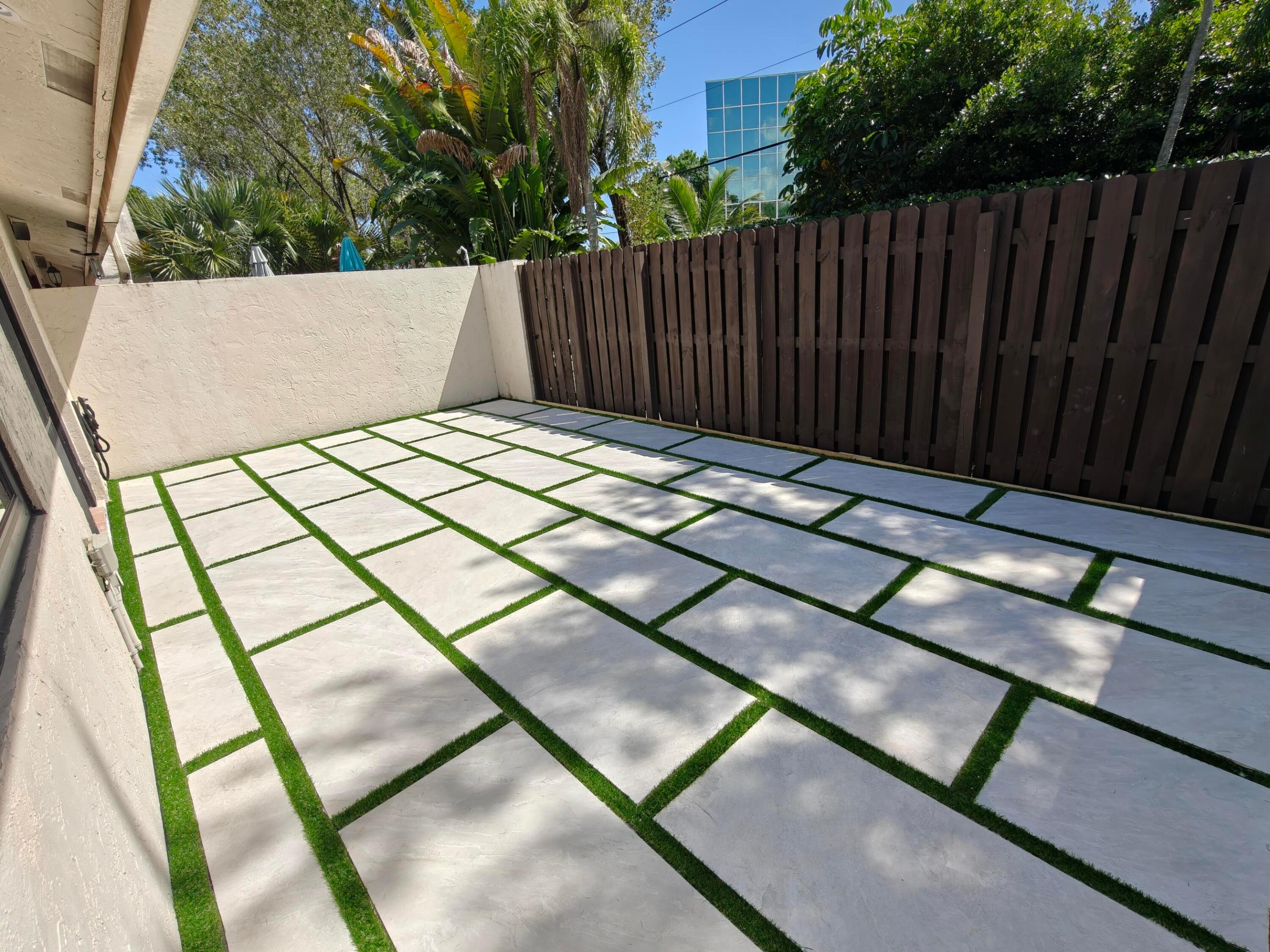 Private courtyard featuring oversized light-toned concrete pavers, synthetic turf ribbons, and vertical wood privacy fencing