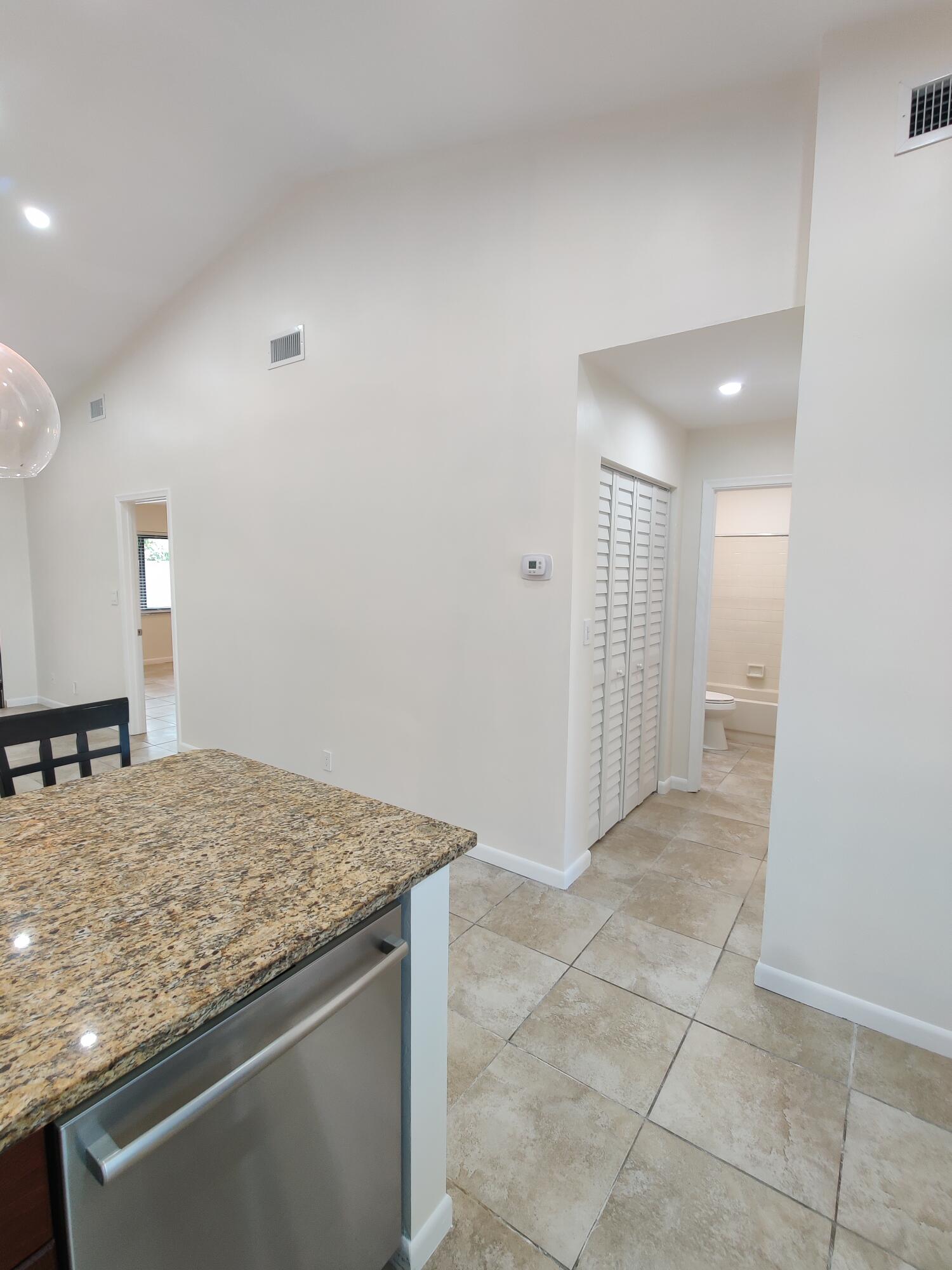Vaulted ceiling, stone-finish countertops, stainless steel appliance, tile flooring, and louvered closet doors