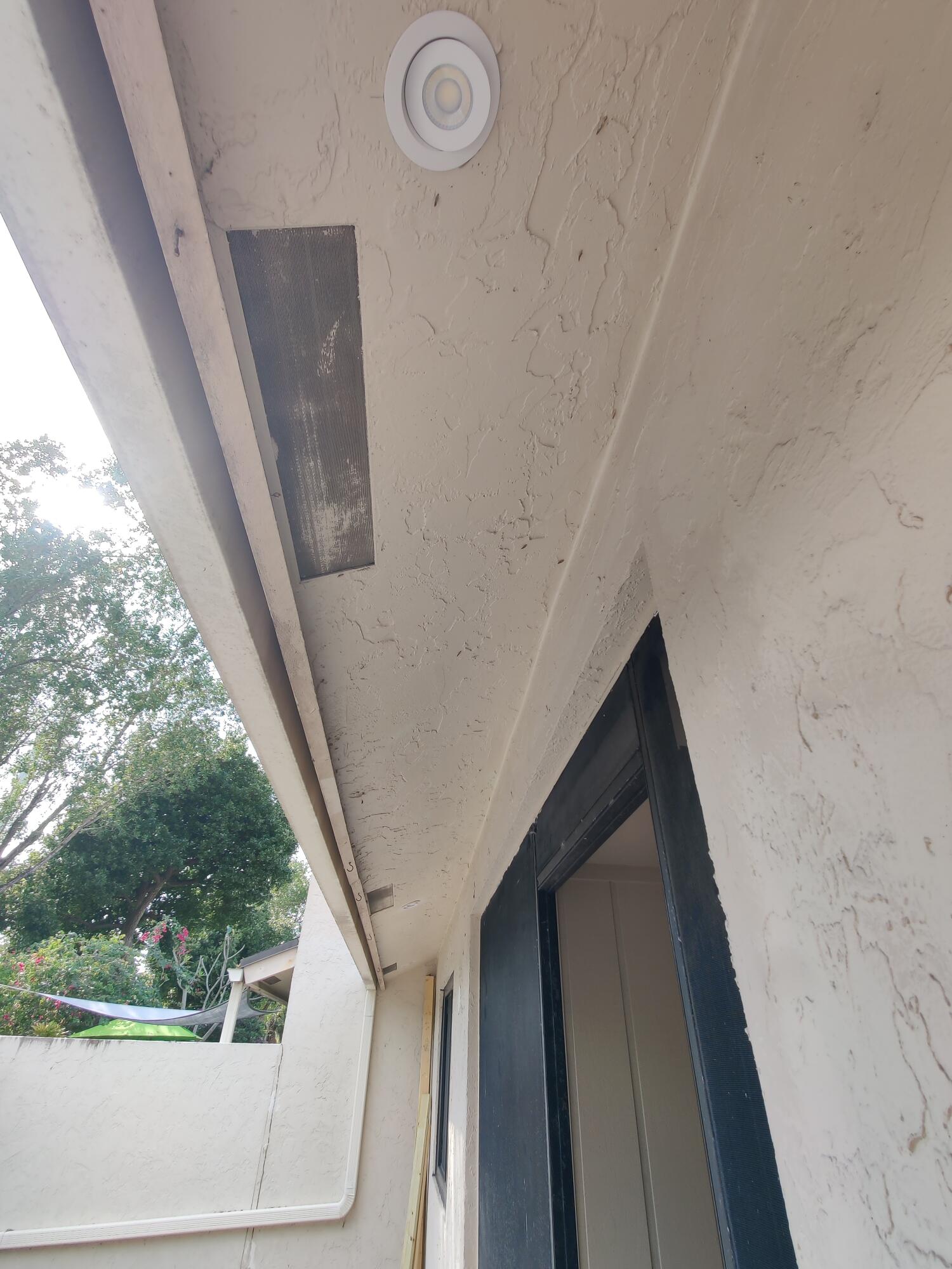 Exterior covered area featuring a textured stucco finish, recessed lighting, and a dark-toned door frame