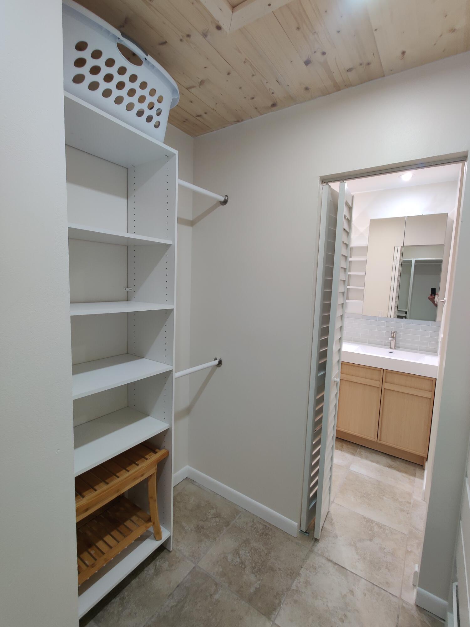 Storage closet featuring white built-in shelving, dual hanging rods, and natural wood-tone ceiling planks, with tile flooring