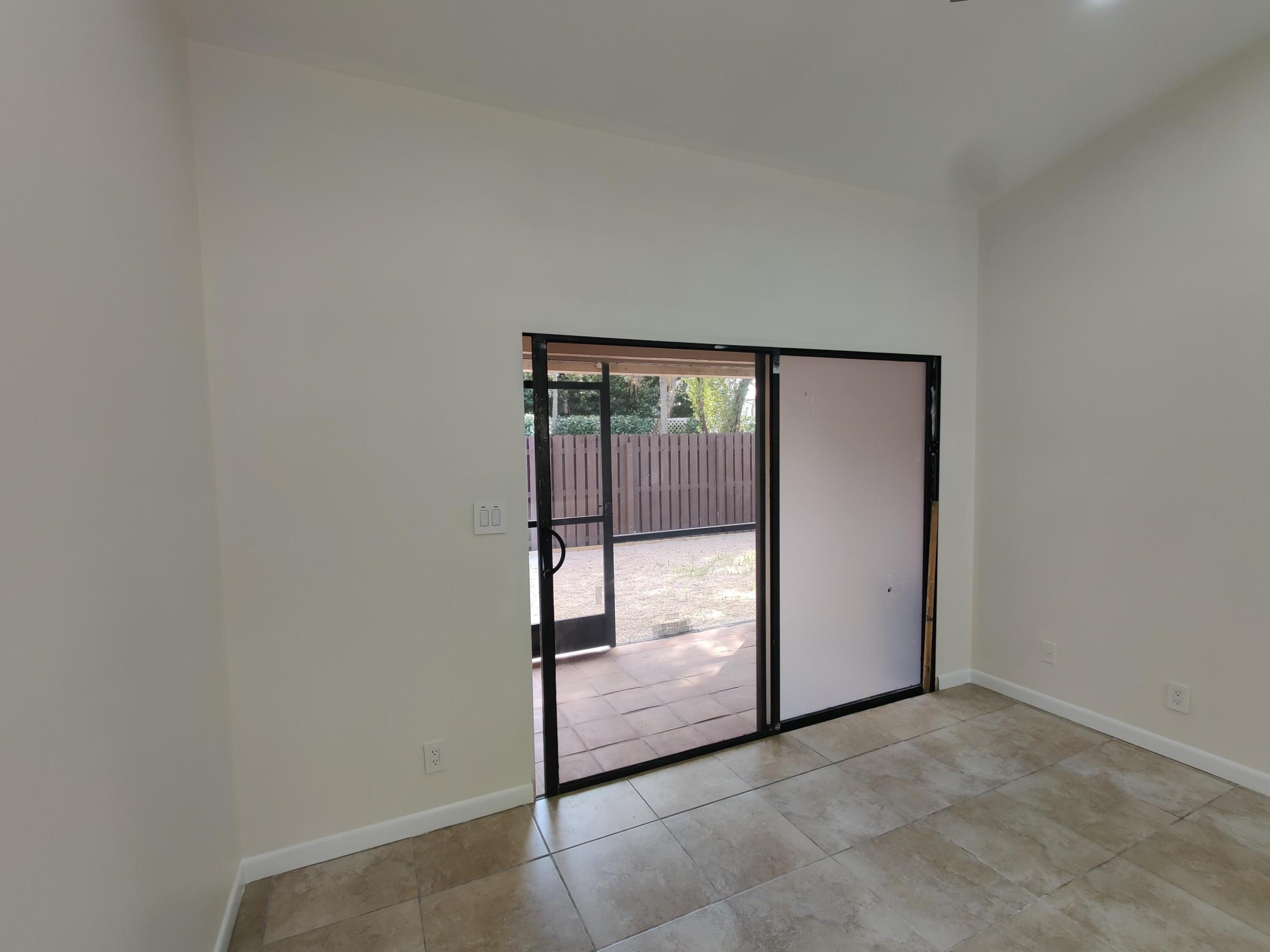 Vaulted ceiling, ceramic tile flooring, and metal-framed sliding glass doors opening to a tiled patio area with a privacy fence