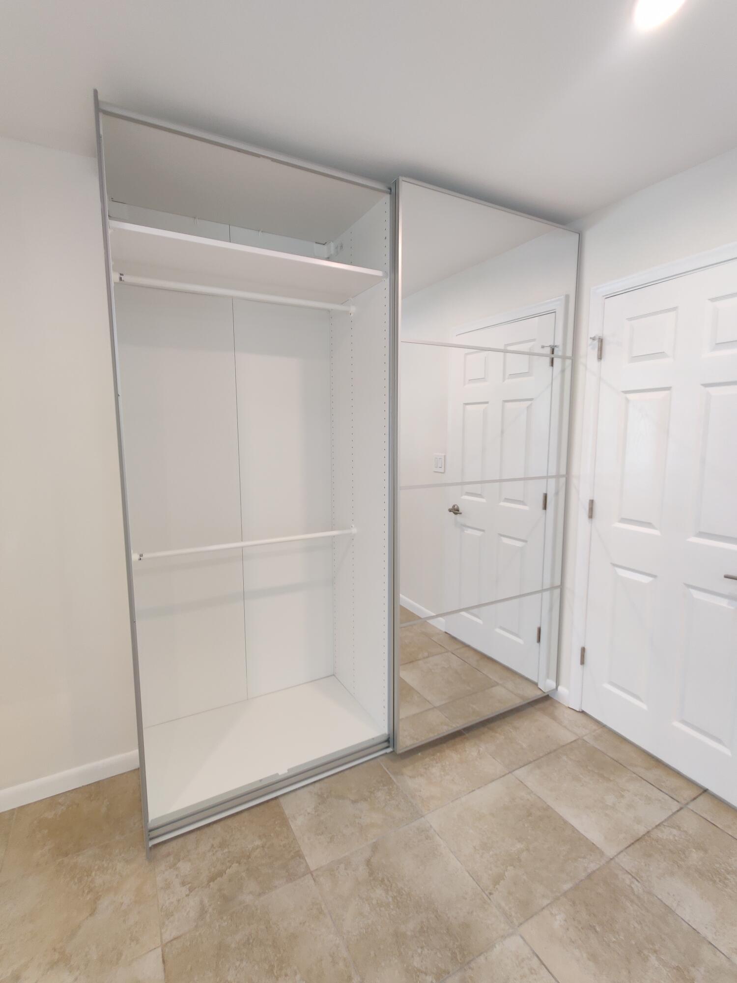 Sliding closet system featuring mirrored panels, integrated shelving, and horizontal hanging rods, complemented by tile flooring