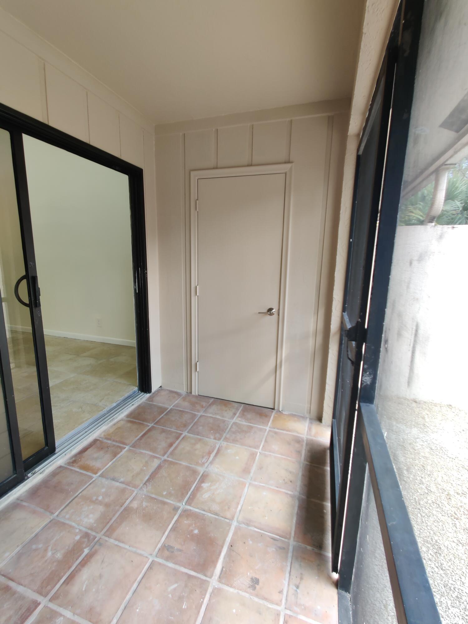 Enclosed porch featuring ceramic tile flooring, vertical wood-paneled walls, a single-panel interior door, and black-framed sliding glass doors