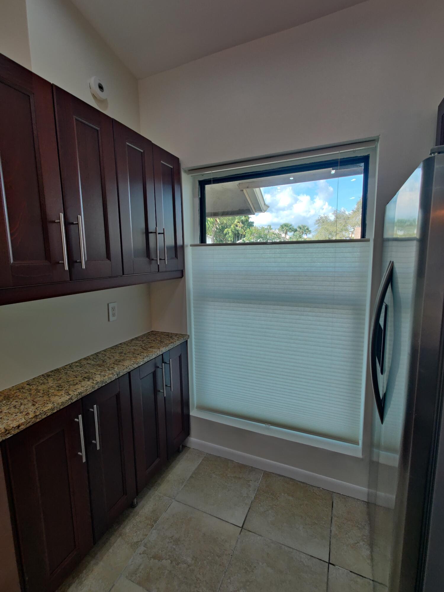 Rich-toned cabinetry featuring satin-finish hardware, stone-surface countertops, and tile flooring