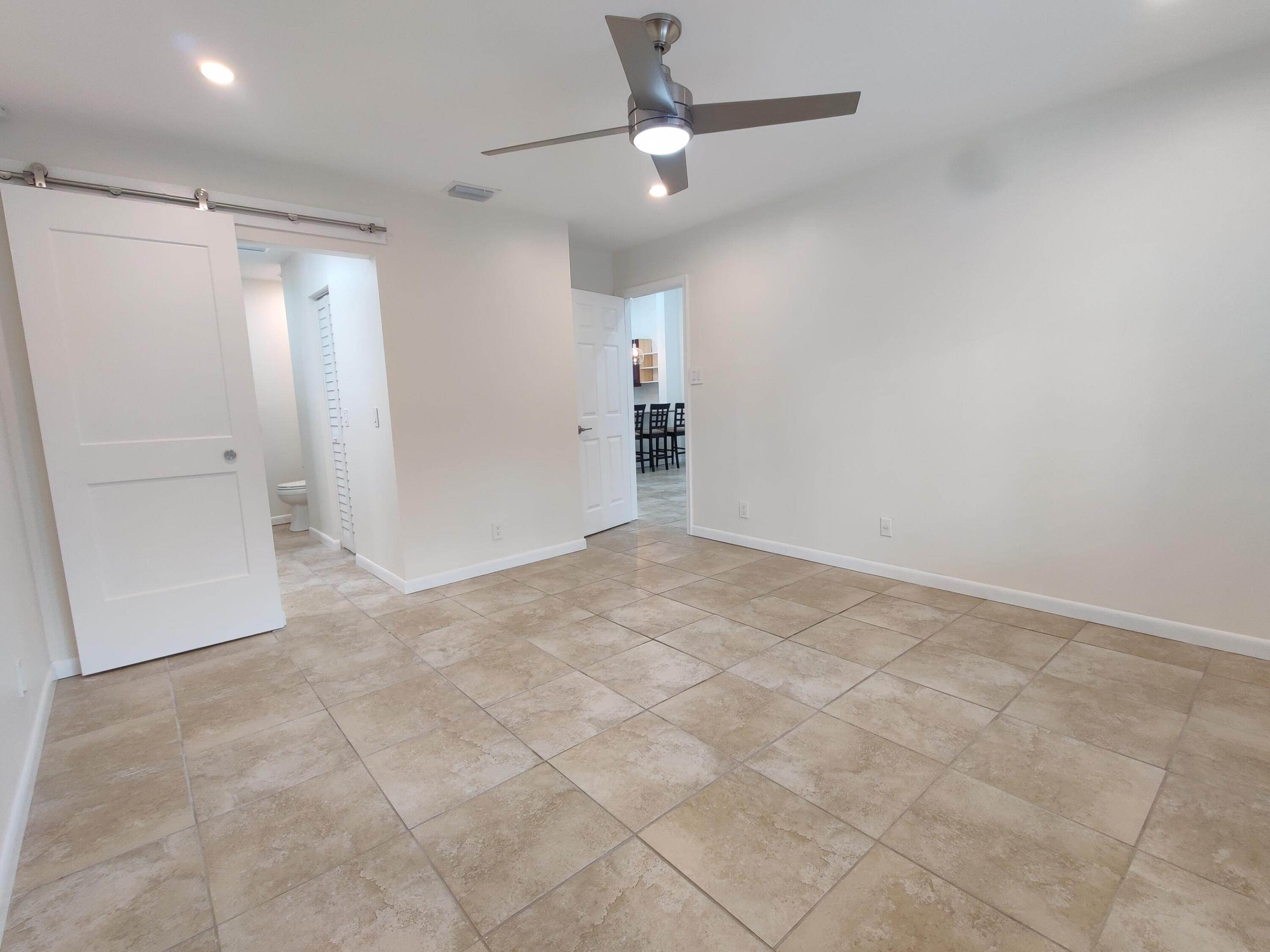 Interior space featuring large-format ceramic tile flooring, a brushed-nickel ceiling fan with integrated lighting, recessed ceiling lights, and a sliding door with exposed stainless steel hardware