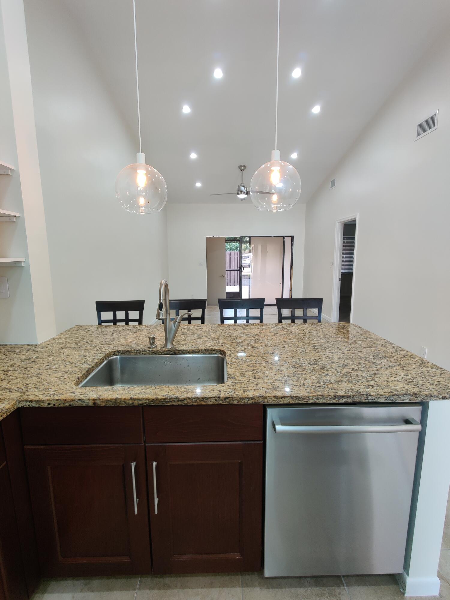 Kitchen island featuring a stone-look countertop, stainless steel undermount sink with a gooseneck faucet, dark wood-finish cabinetry, stainless steel dishwasher, and dual glass globe pendant lights