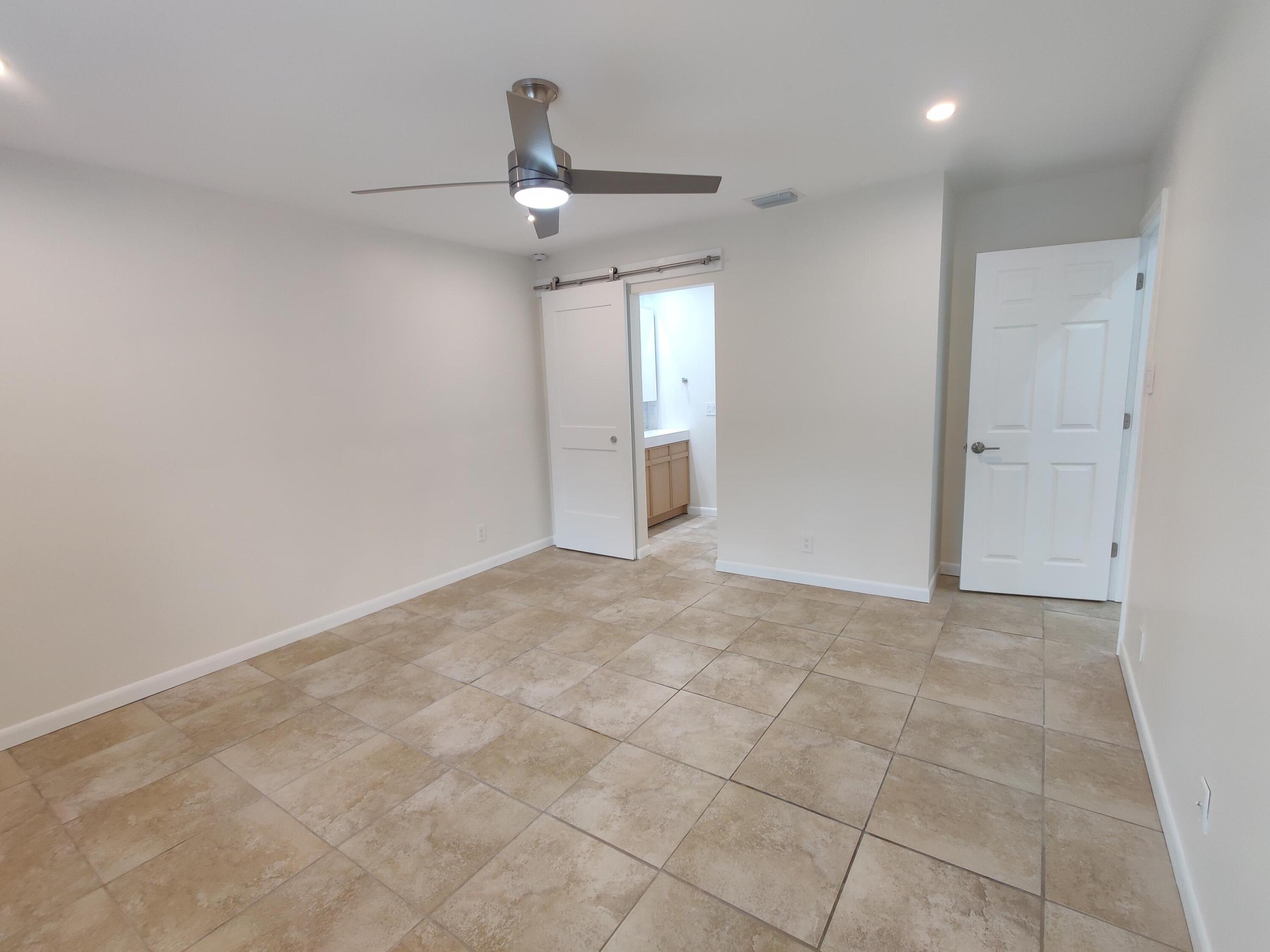 Neutral-toned tile flooring, brushed metal ceiling fan with integrated lighting, sliding barn-style door, and paneled interior door