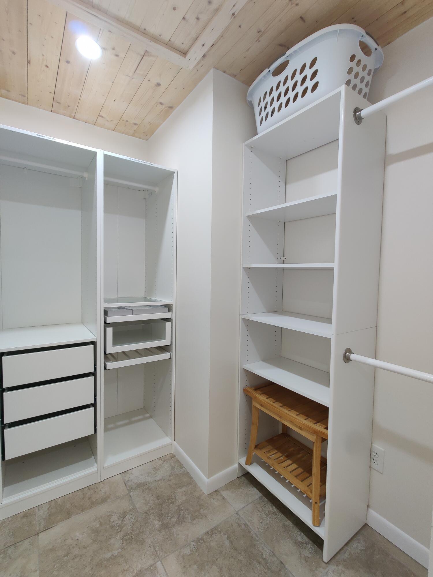 Walk-in closet featuring white built-in shelving, integrated dresser drawers, dual hanging rods, and wood-plank ceiling finish with tile flooring