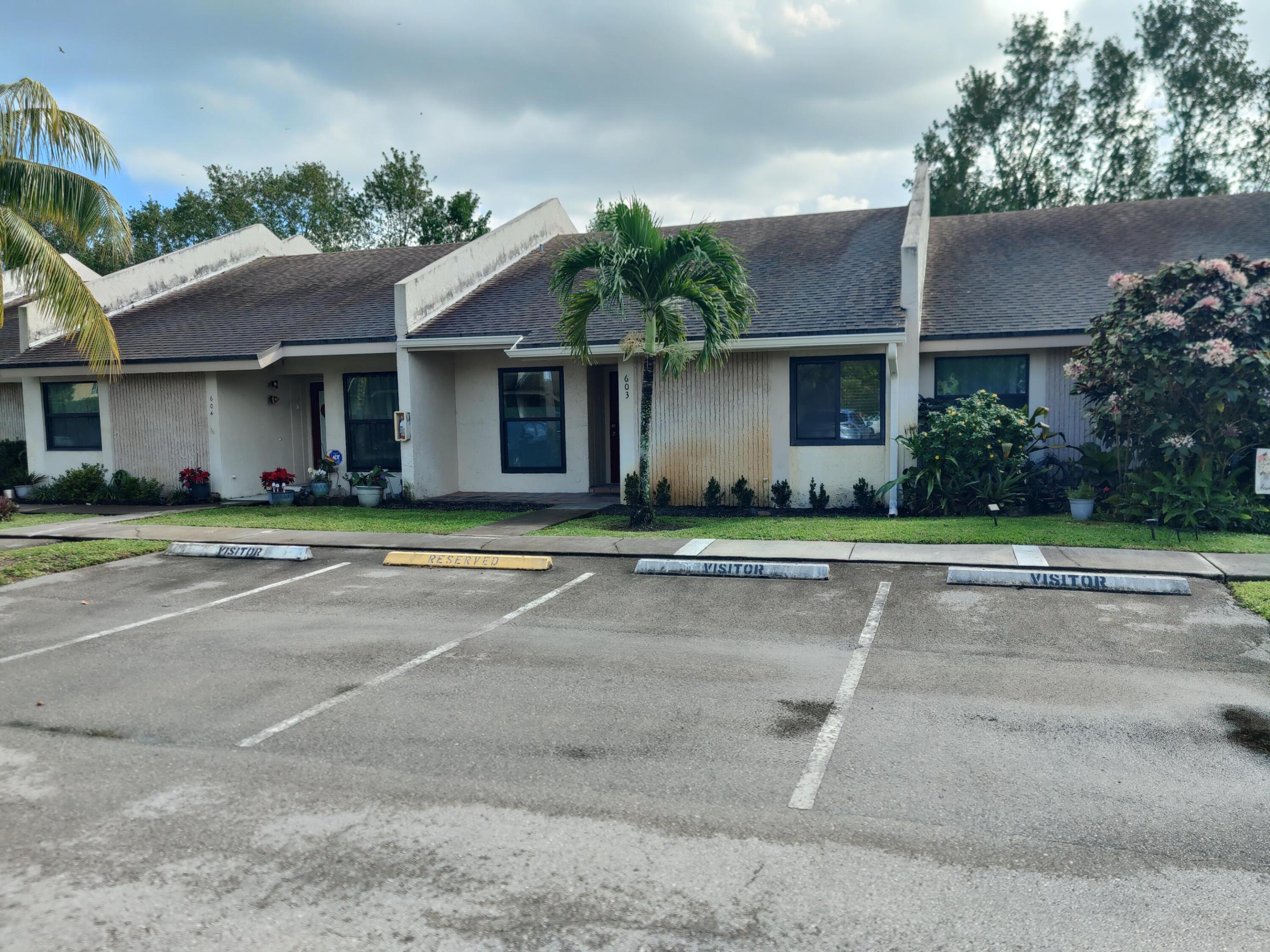 Single-story exterior featuring light-colored stucco siding, asphalt shingle roofing, and dedicated parking spaces