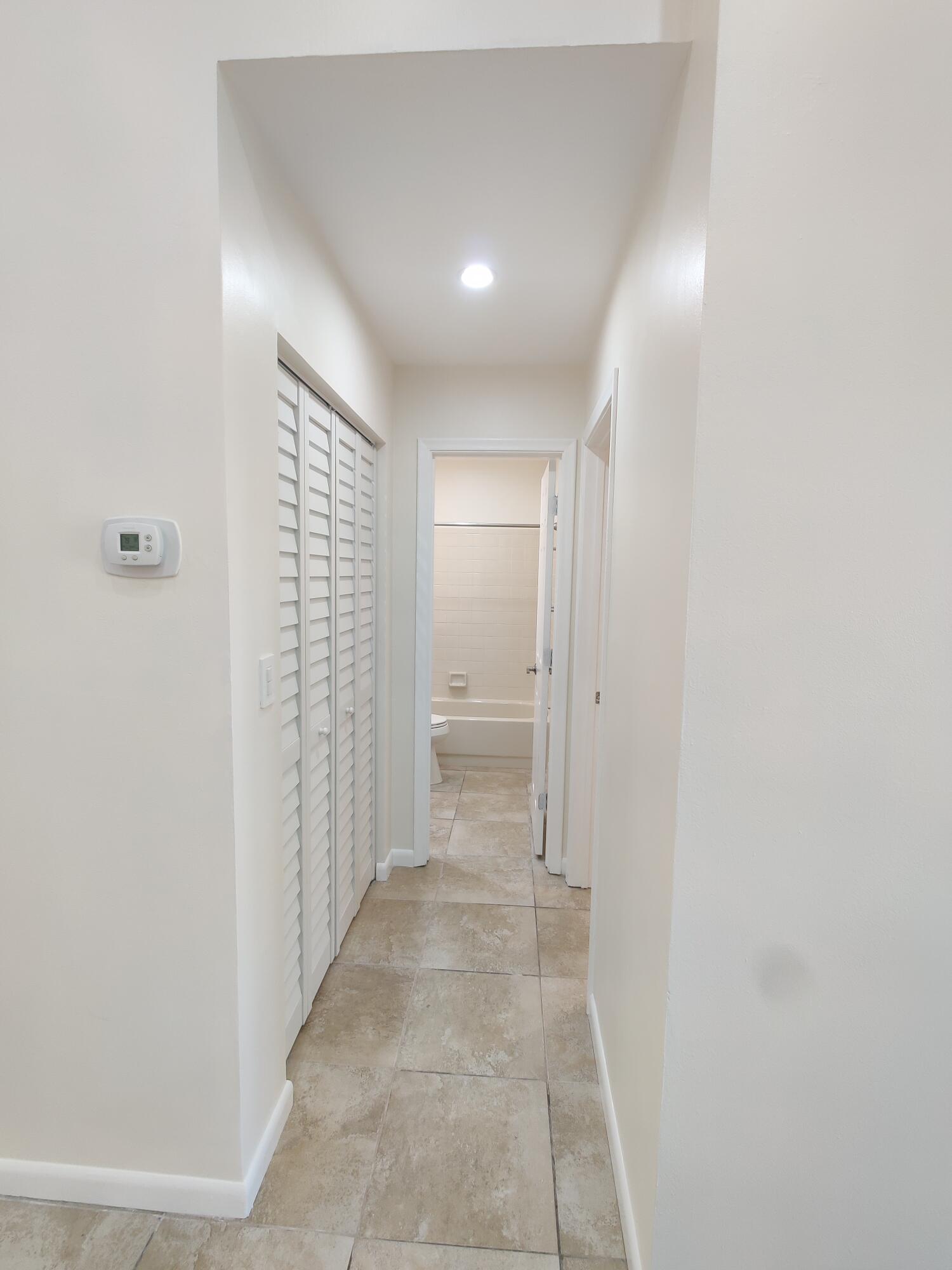 Hallway featuring large-format ceramic tile flooring, recessed ceiling lighting, and floor-to-ceiling louvered bi-fold closet doors