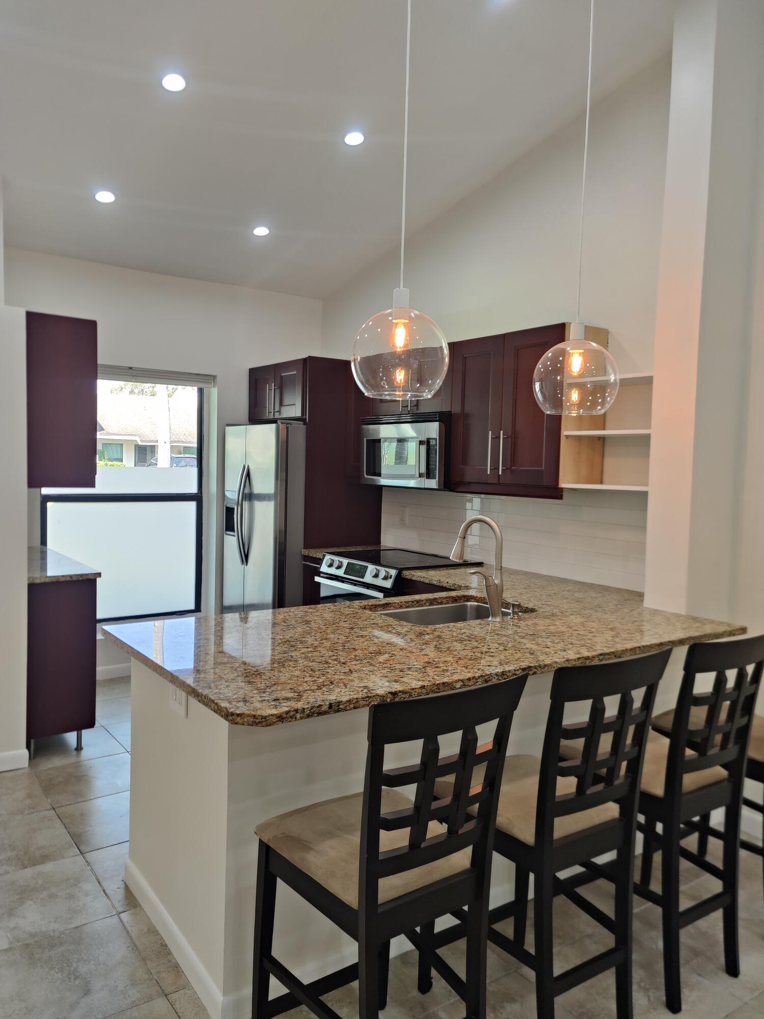 Kitchen featuring dark wood cabinetry, stone-surface countertops, stainless steel appliances, dual glass globe pendant lights, and tile flooring