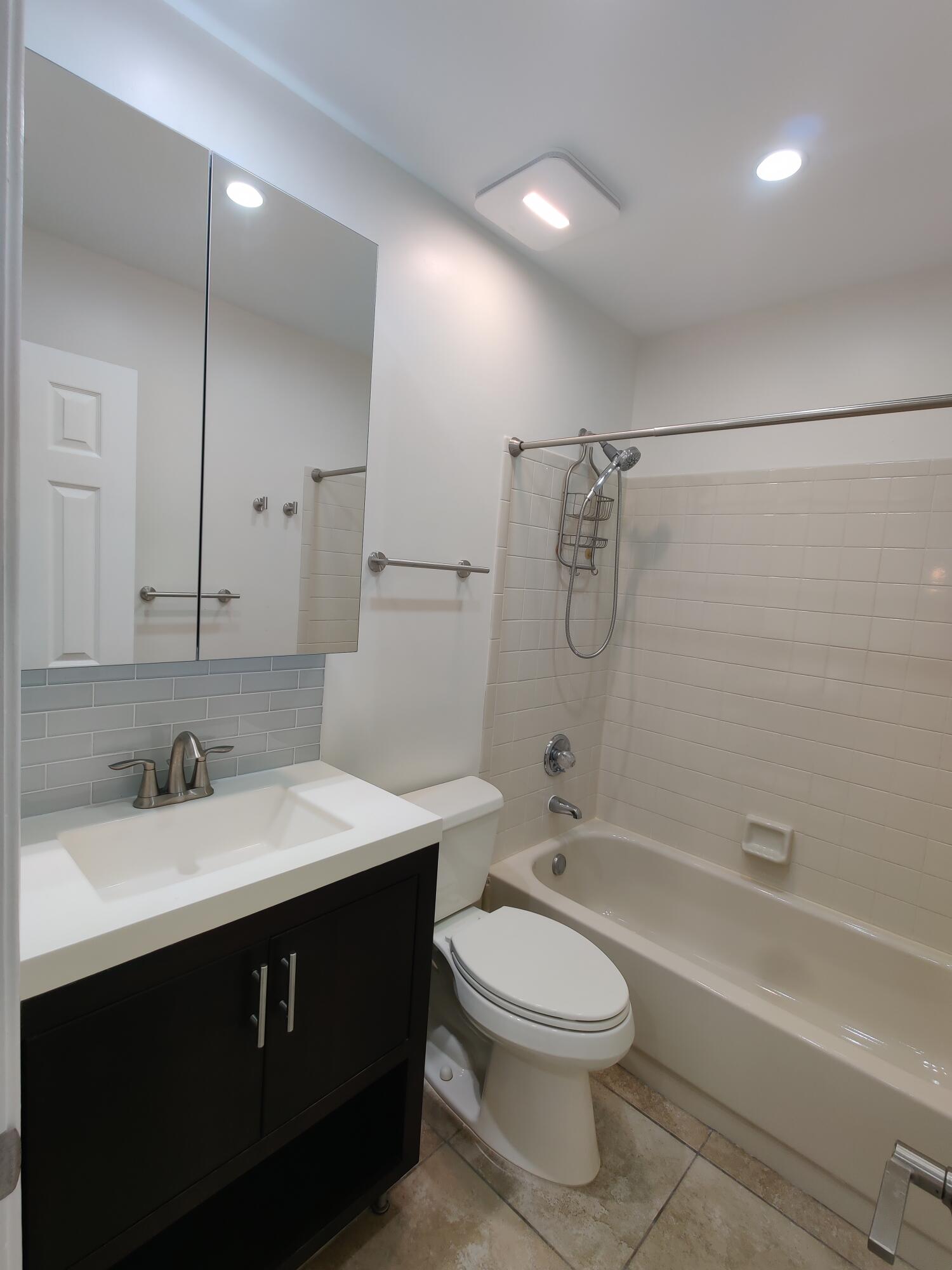 Bathroom featuring a vanity with a white countertop and rectangular basin, a mirrored medicine cabinet, a tiled tub-shower combination, and recessed lighting