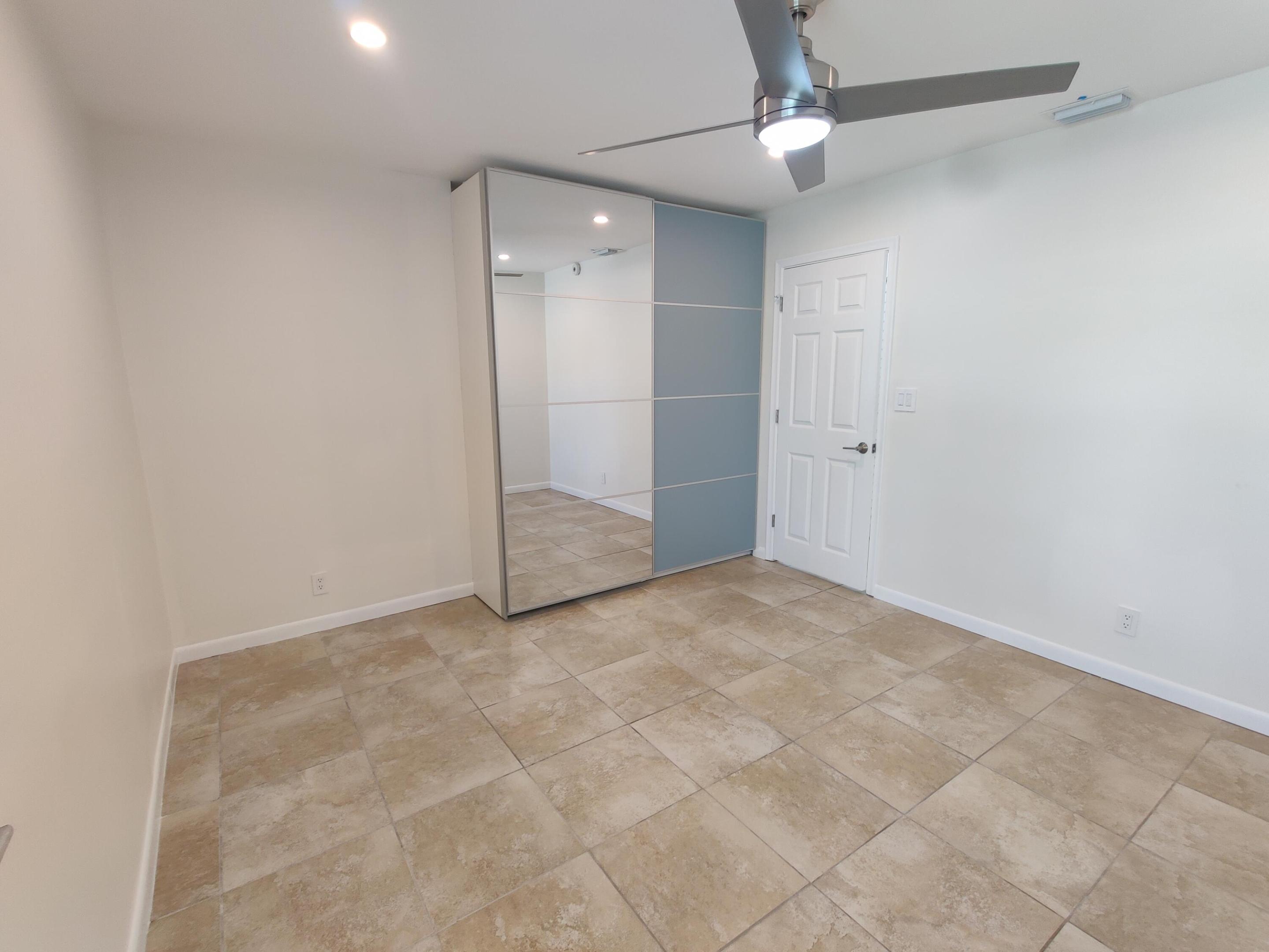 Large-format tile flooring, built-in floor-to-ceiling wardrobe with mirrored and sliding panels, and a modern brushed-metal ceiling fan with integrated lighting
