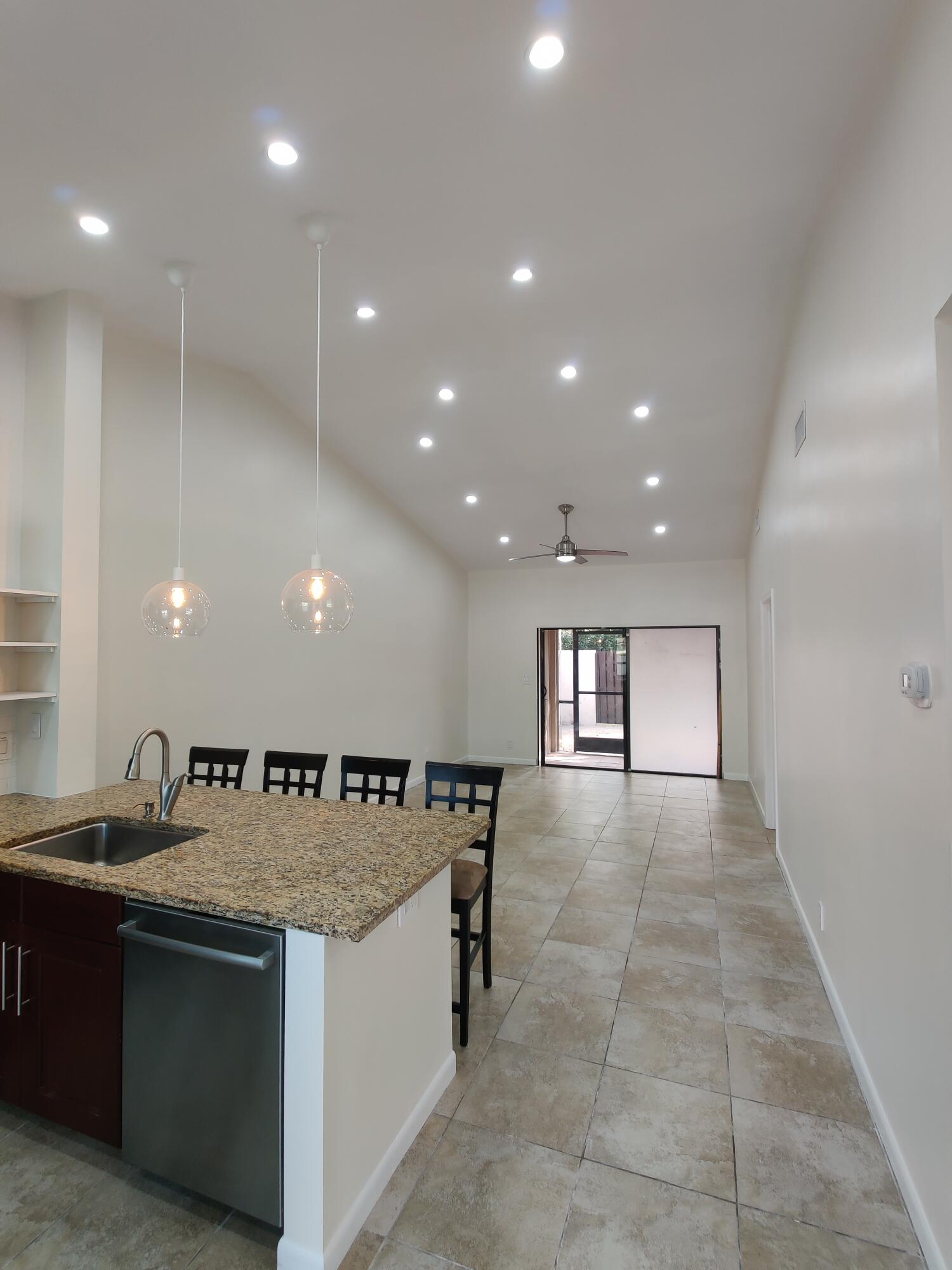 Open-concept interior featuring vaulted ceilings, recessed lighting, tile flooring, a kitchen island with a stone countertop, and two glass pendant lights