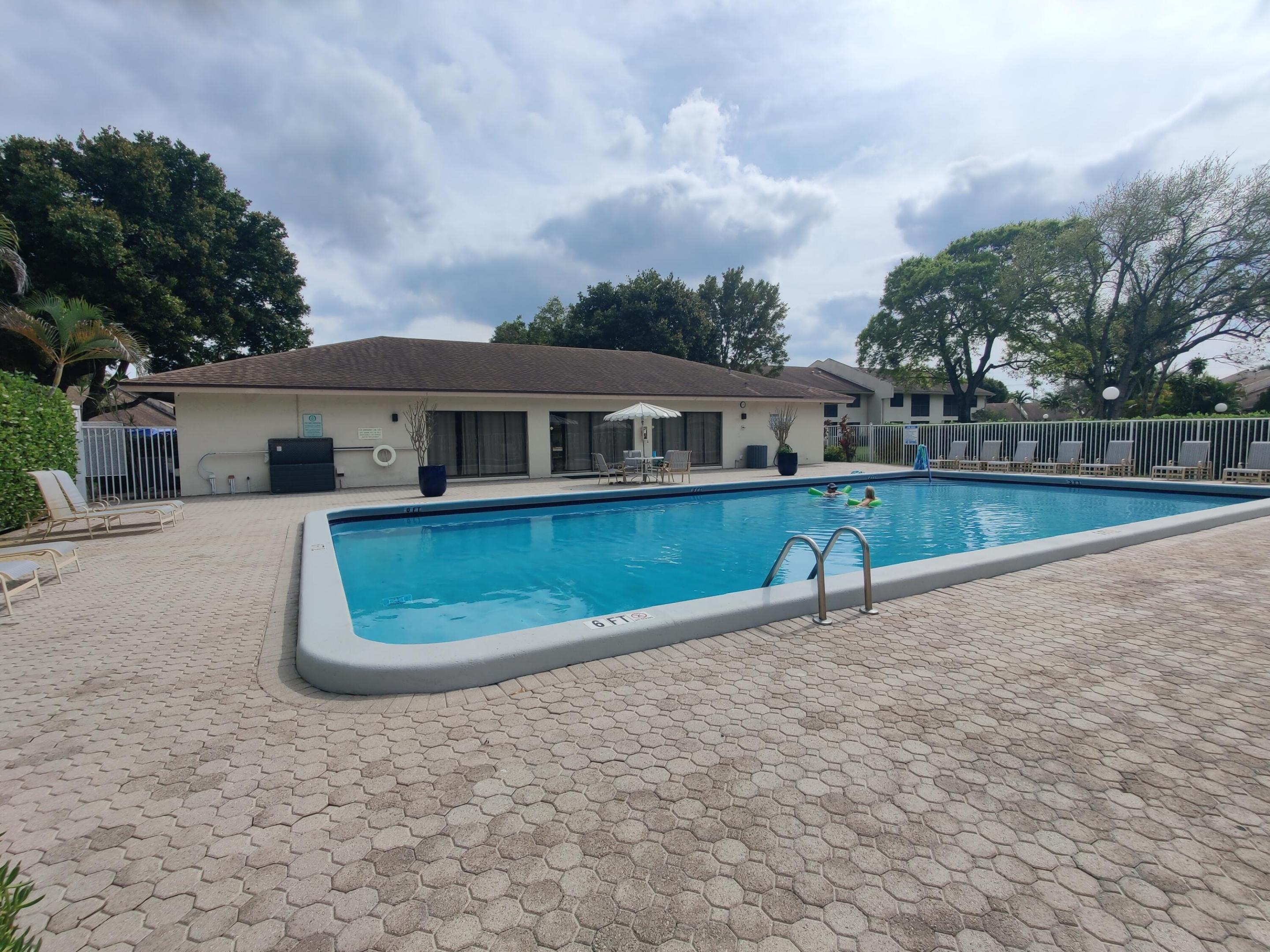 Rectangular swimming pool featuring a concrete surround, metal entry ladder, expansive paver decking, and perimeter fencing