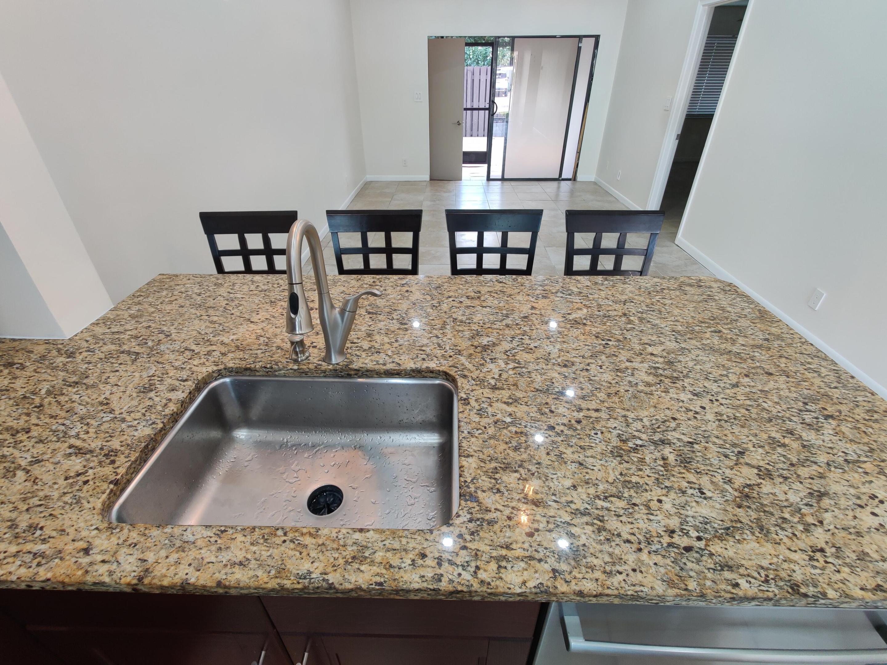 Kitchen island featuring a stone-look countertop, stainless steel undermount sink, and high-arc pull-down faucet