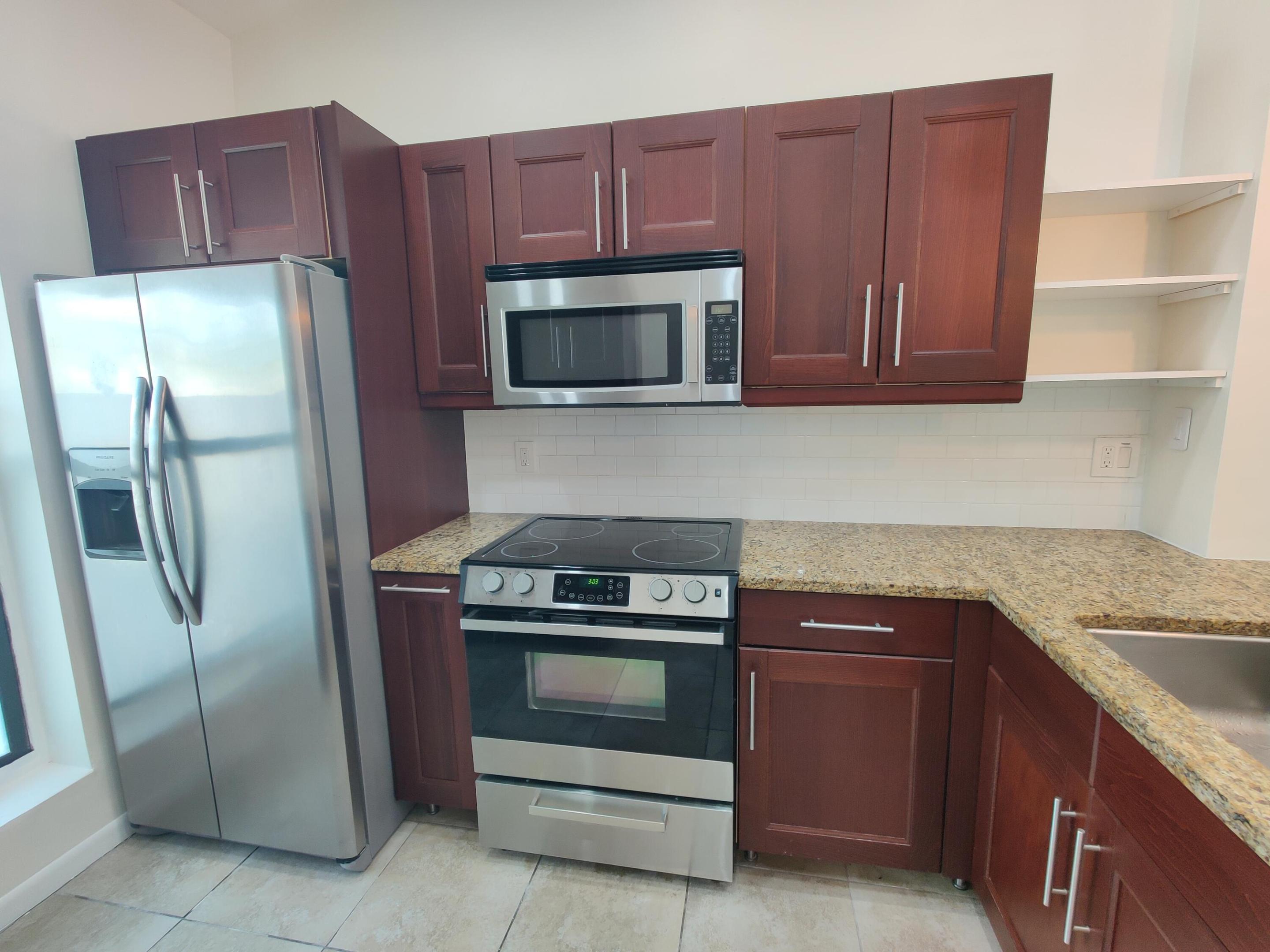 Kitchen featuring wood-finish cabinetry, stone-surface countertops, stainless steel appliances, and built-in shelving