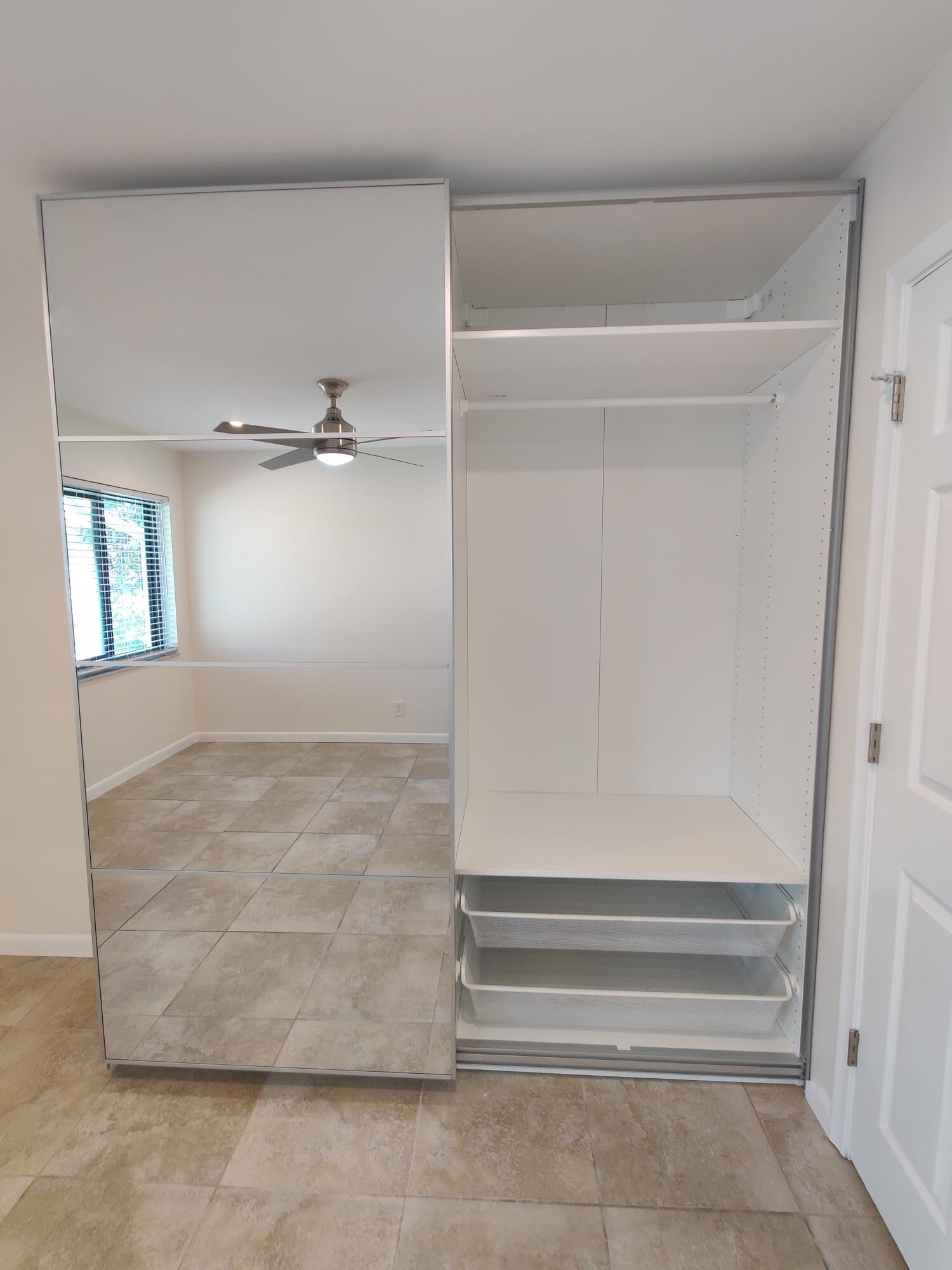Built-in floor-to-ceiling wardrobe featuring mirrored sliding doors, interior shelving, a hanging rod, and two pull-out drawers