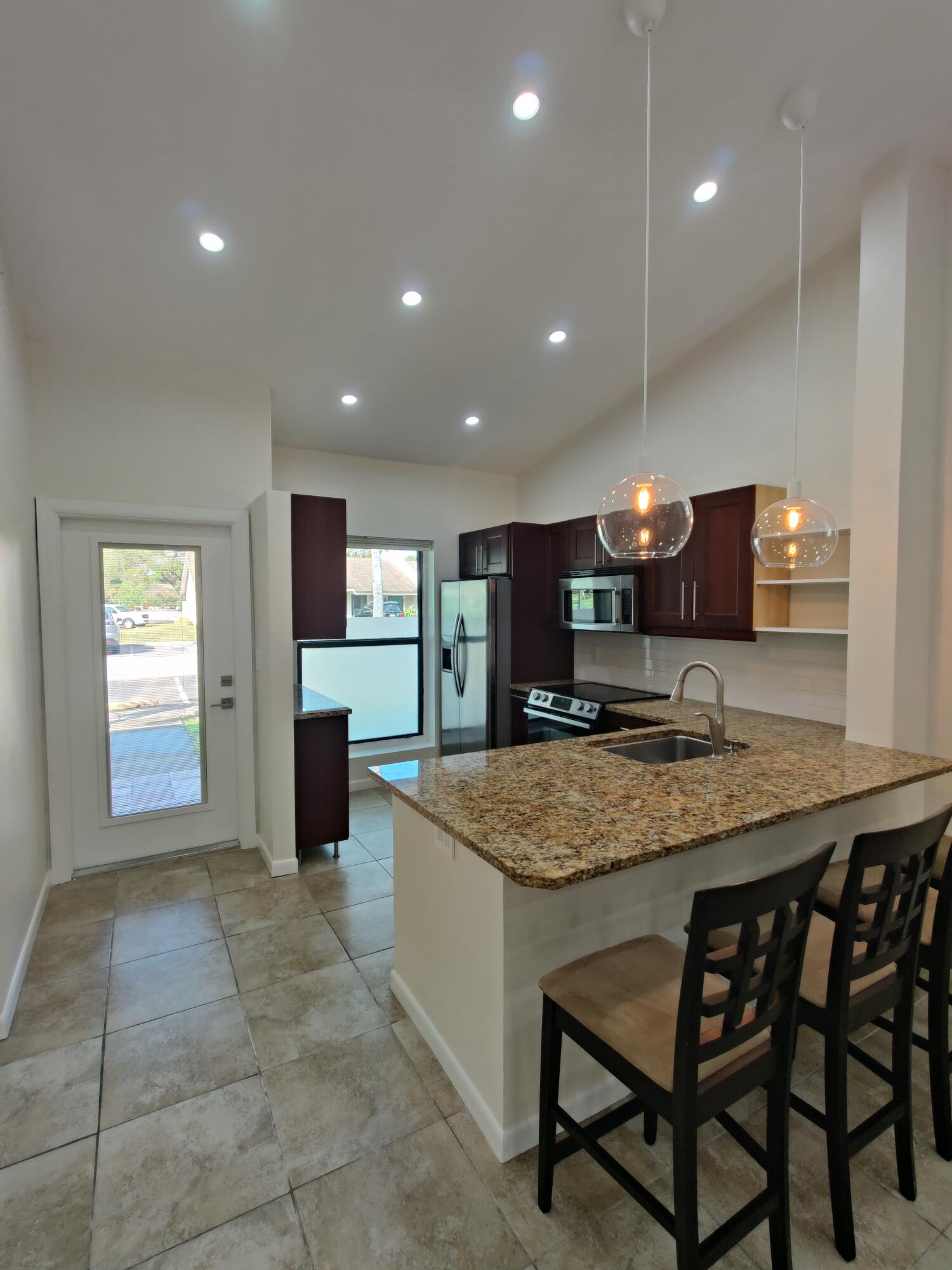 Kitchen featuring a stone-topped island with an integrated sink, dark wood cabinetry, recessed lighting, glass globe pendant fixtures, and neutral tile flooring