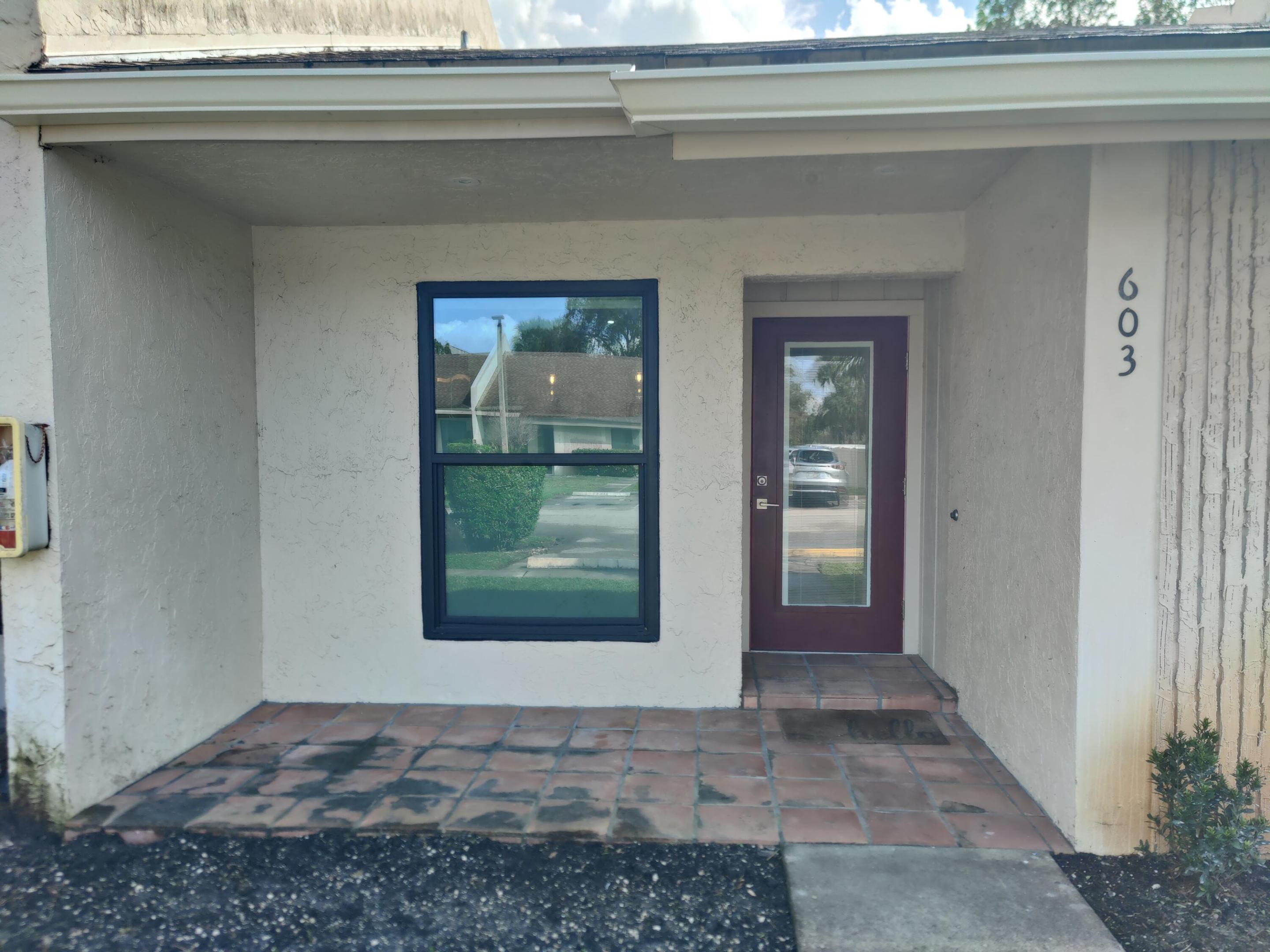 Covered entrance featuring stucco exterior, terracotta-style tiled porch, single-light glass panel entry door, and dark-framed windows