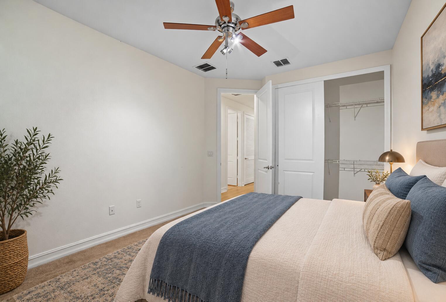 Neutral interior room featuring a ceiling fan with wood-finish blades, a multi-panel interior door, and a built-in closet with wire shelving