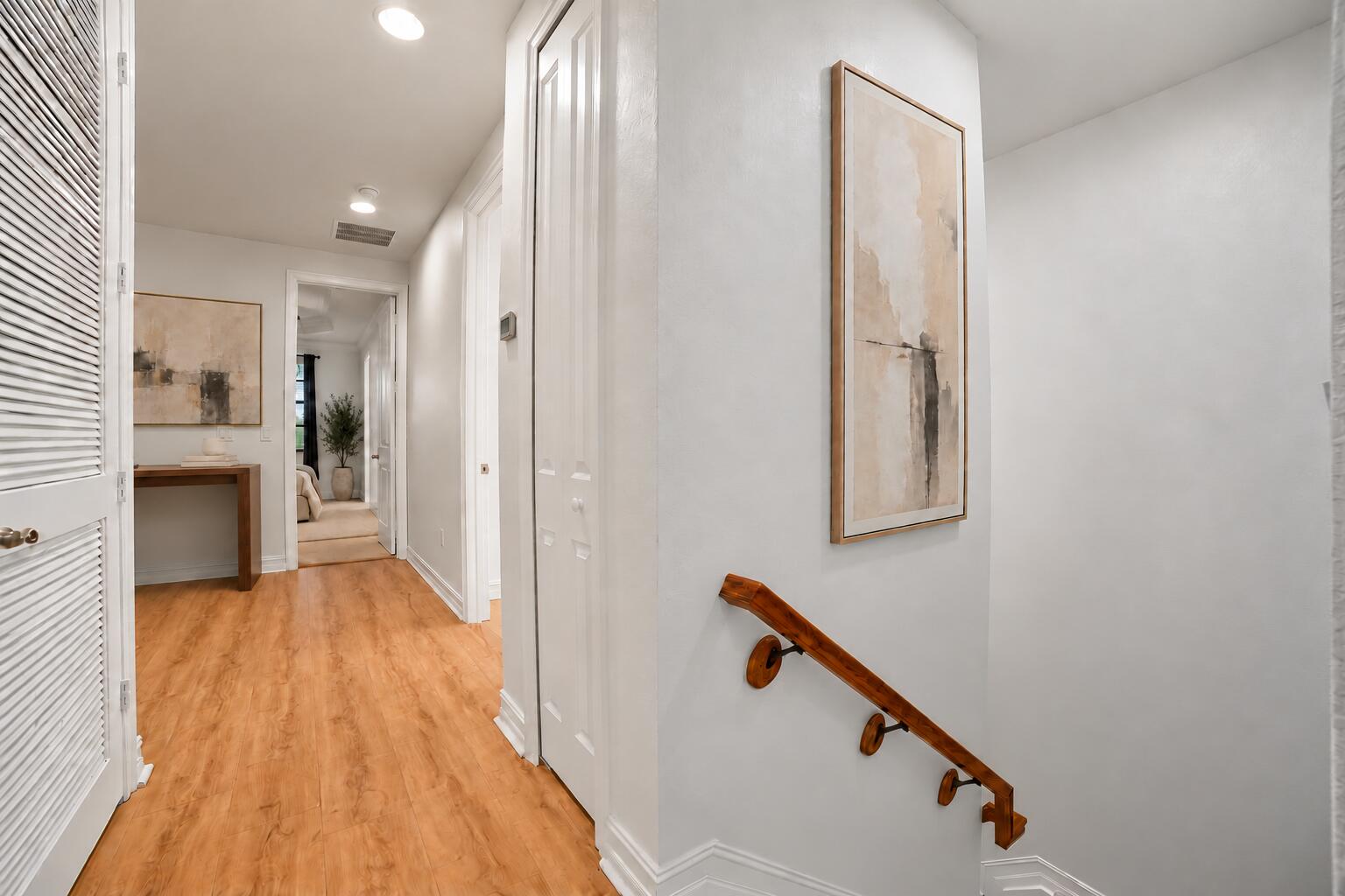 Hallway featuring wood-finish flooring, white louvered doors, recessed ceiling lighting, and a wood-mounted handrail