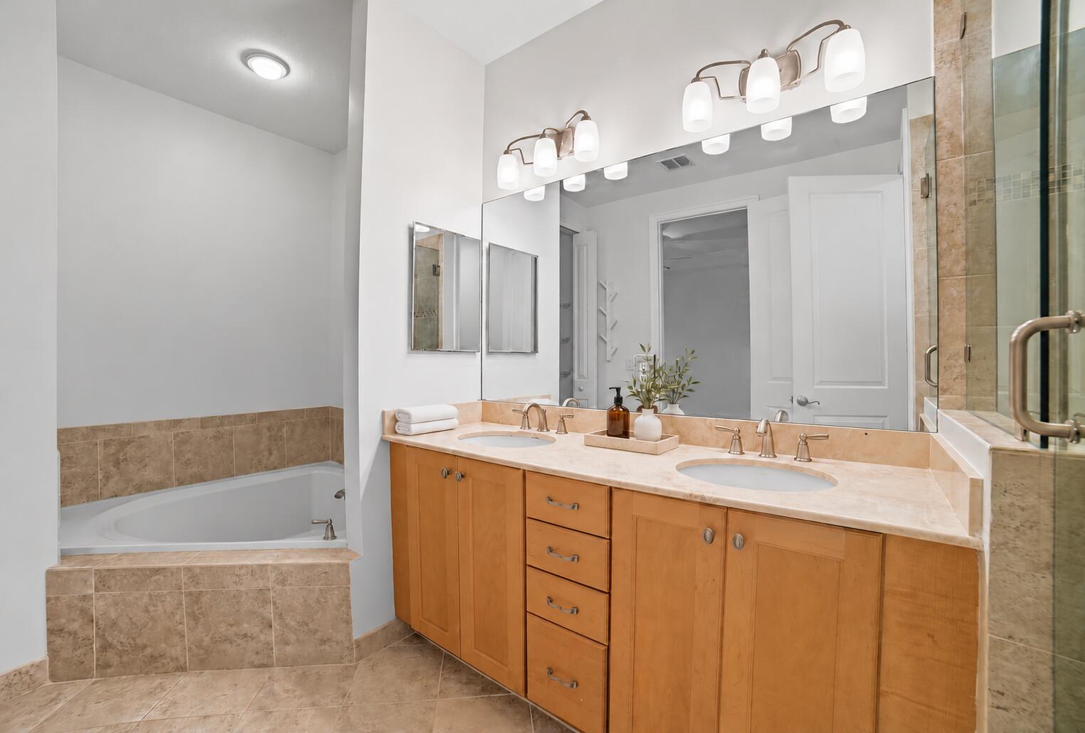 Dual-vanity cabinetry with stone-finish countertops, drop-in sinks, recessed lighting, and a tile-surround soaking tub
