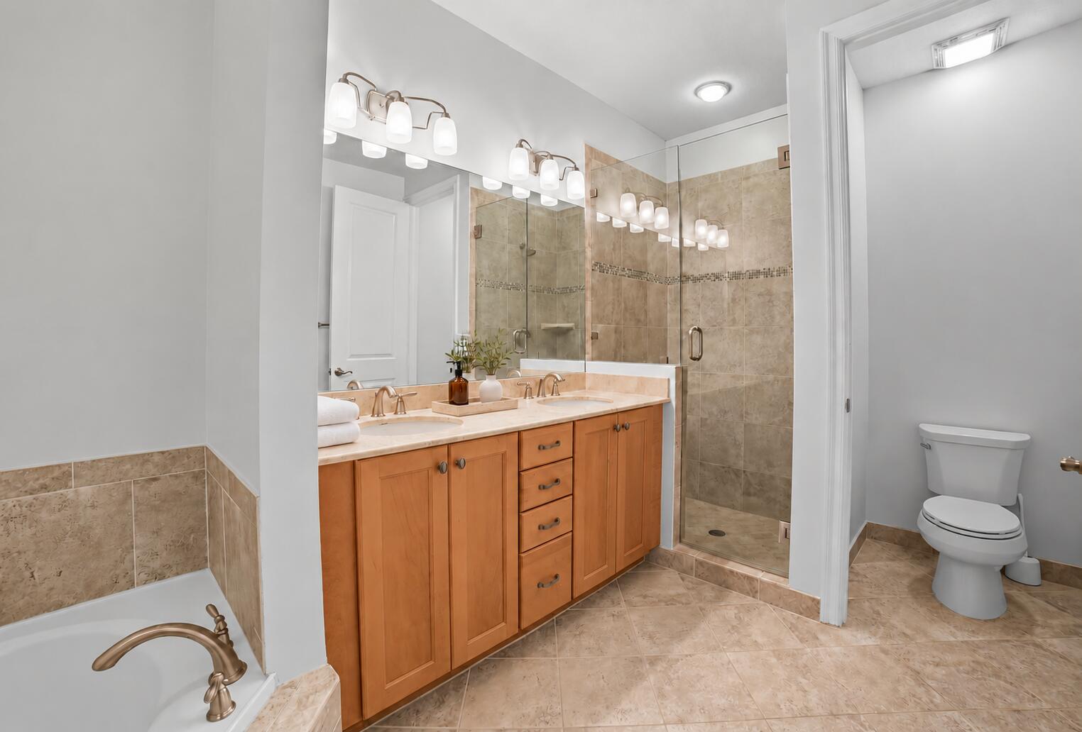 Bathroom featuring a dual-sink vanity with wood cabinetry, a tiled glass-enclosed shower, a deep soaking tub, and large-format tile flooring