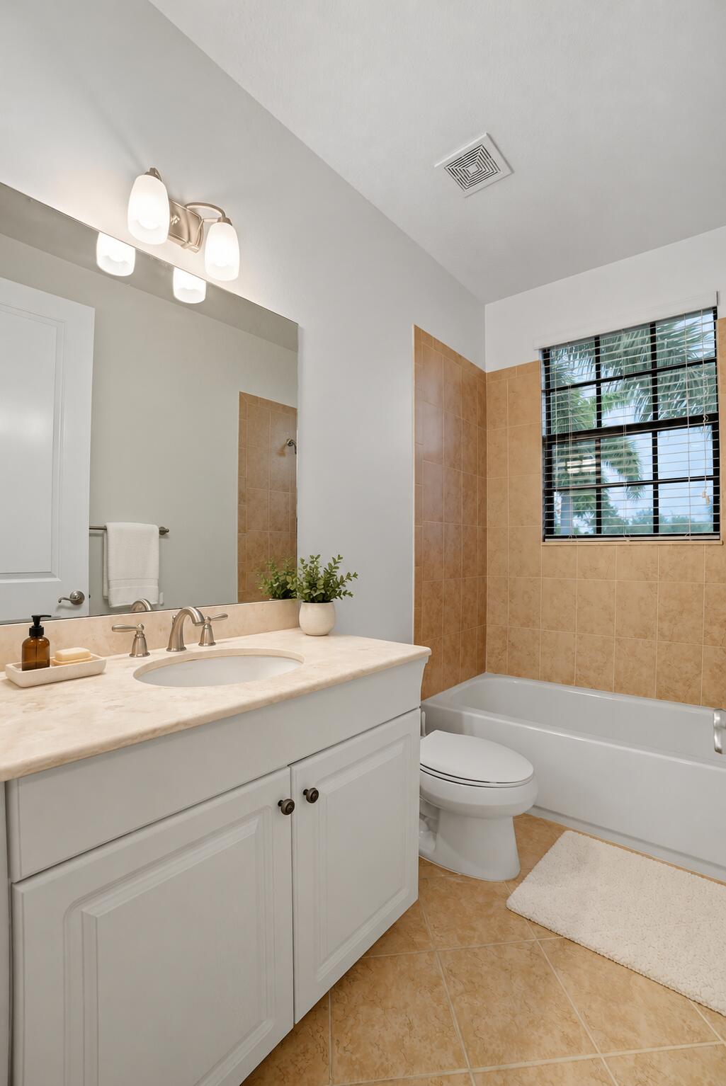 White cabinetry with a stone-top vanity, undermount sink, three-light polished chrome fixture, and tiled tub surround