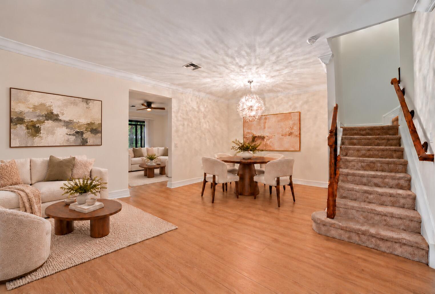 Open-concept area featuring wood-finish flooring, crown molding, a spherical pendant light fixture, and a staircase with a natural wood handrail