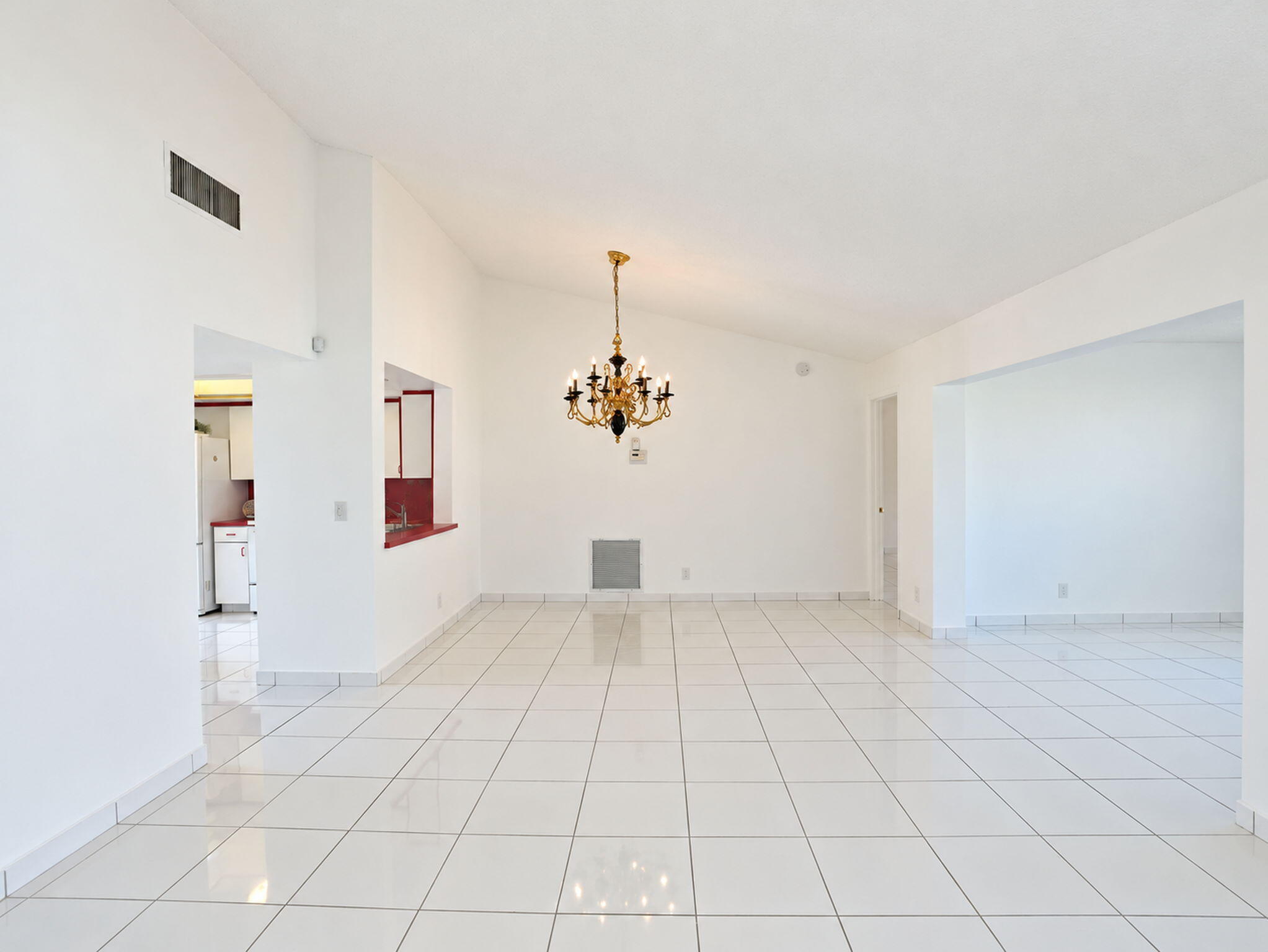 Vaulted ceilings, polished white tile flooring, and a decorative multi-arm chandelier