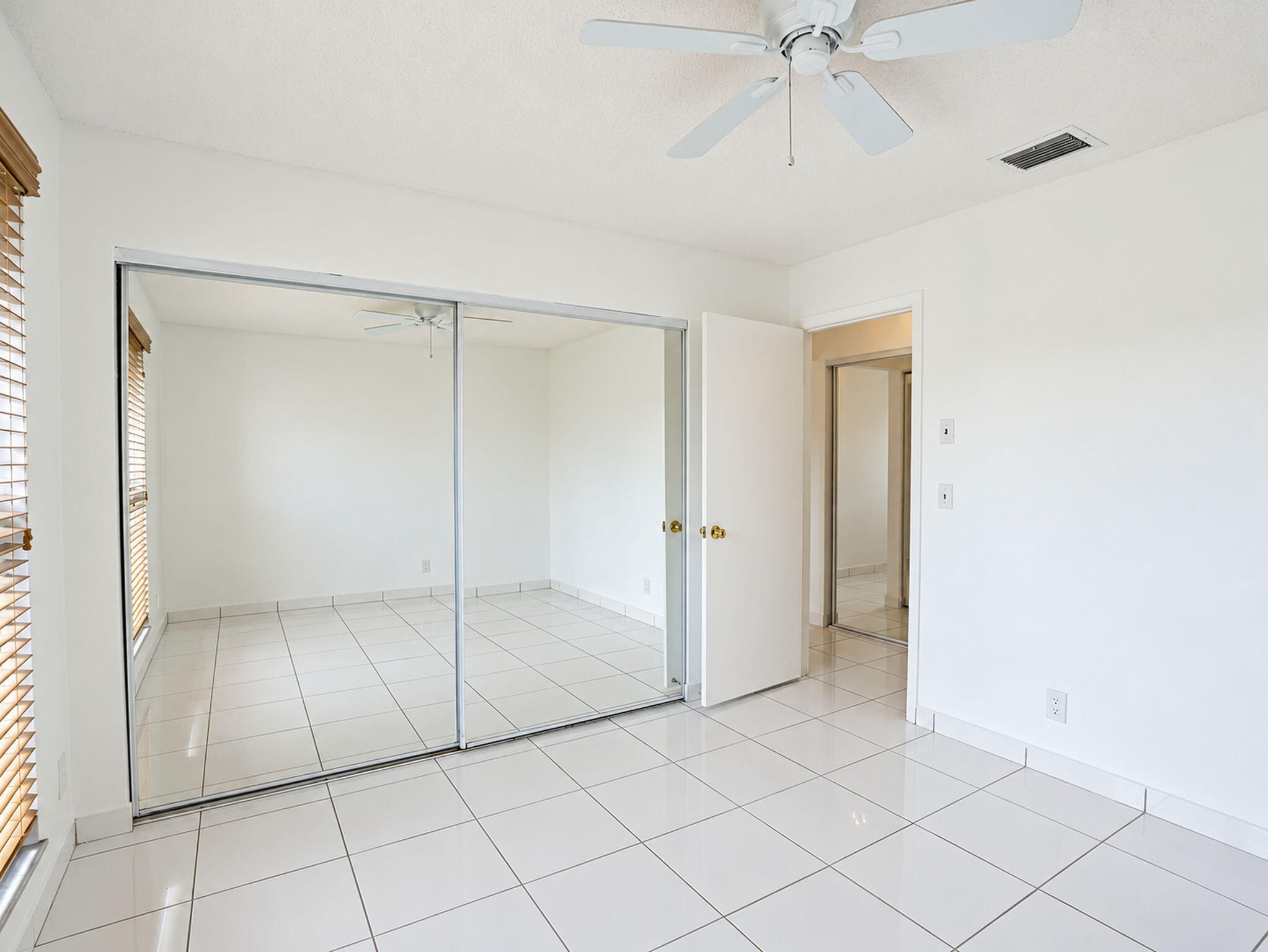 Tile flooring, sliding mirrored closet doors, ceiling fan, and window blinds