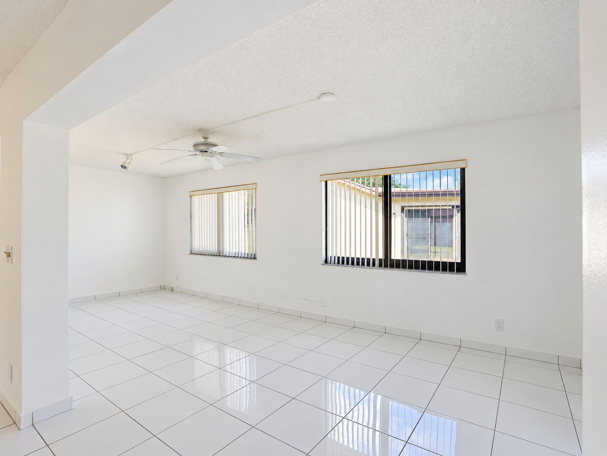 White tile flooring, dual windows with vertical blinds, and ceiling-mounted track lighting and fan