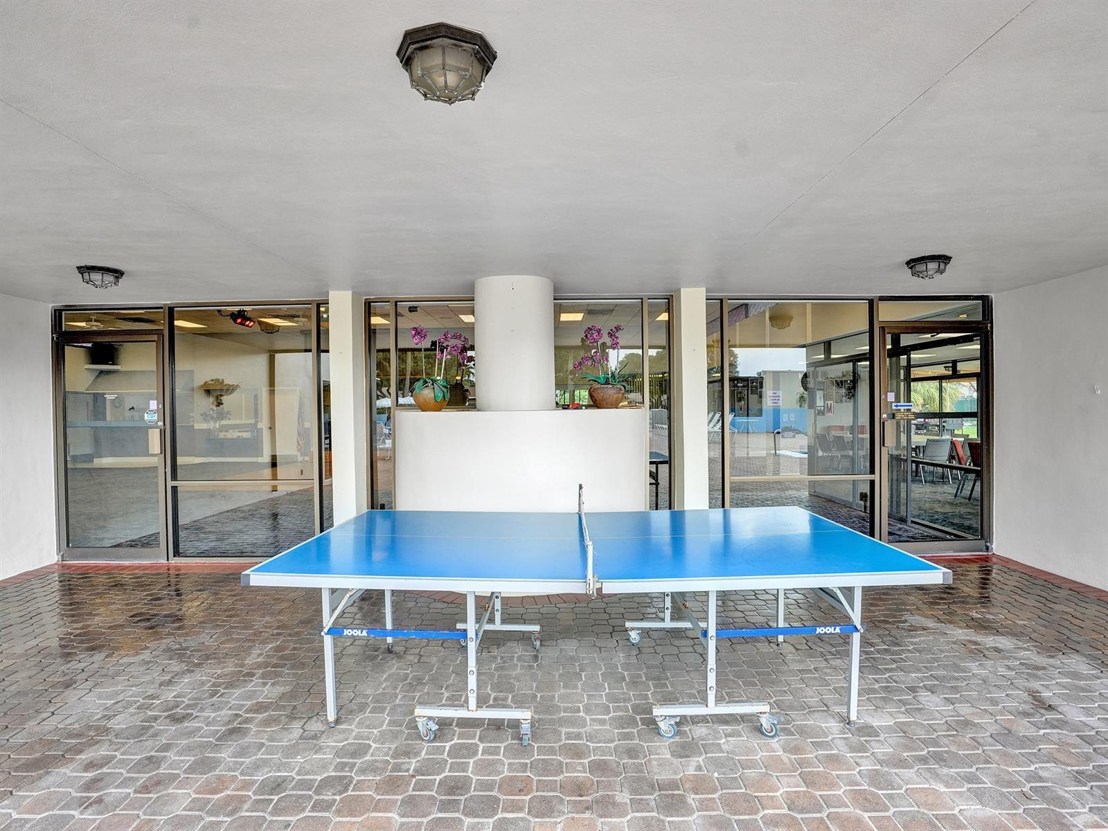 Covered patio featuring stone-paver flooring, extensive floor-to-ceiling glass paneling, and ceiling-mounted light fixtures