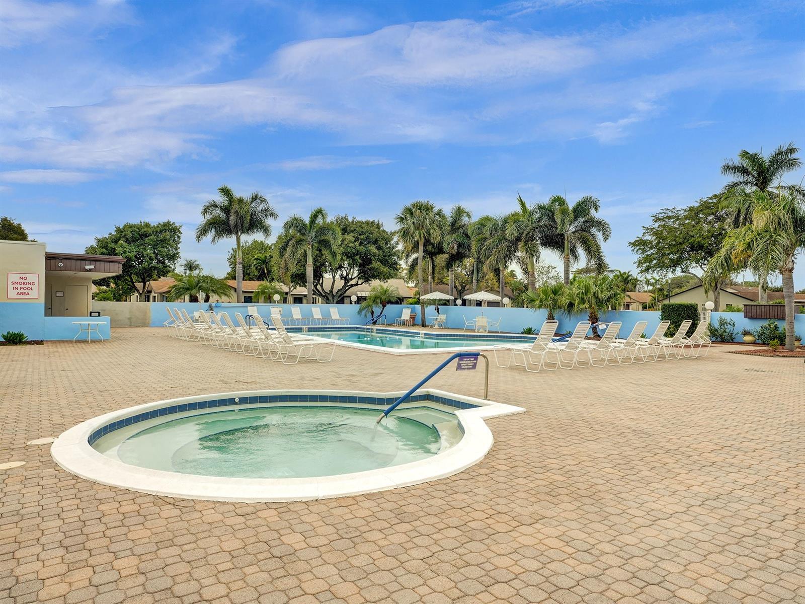 Outdoor community pool area featuring a built-in spa, paved decking, and mature palm trees