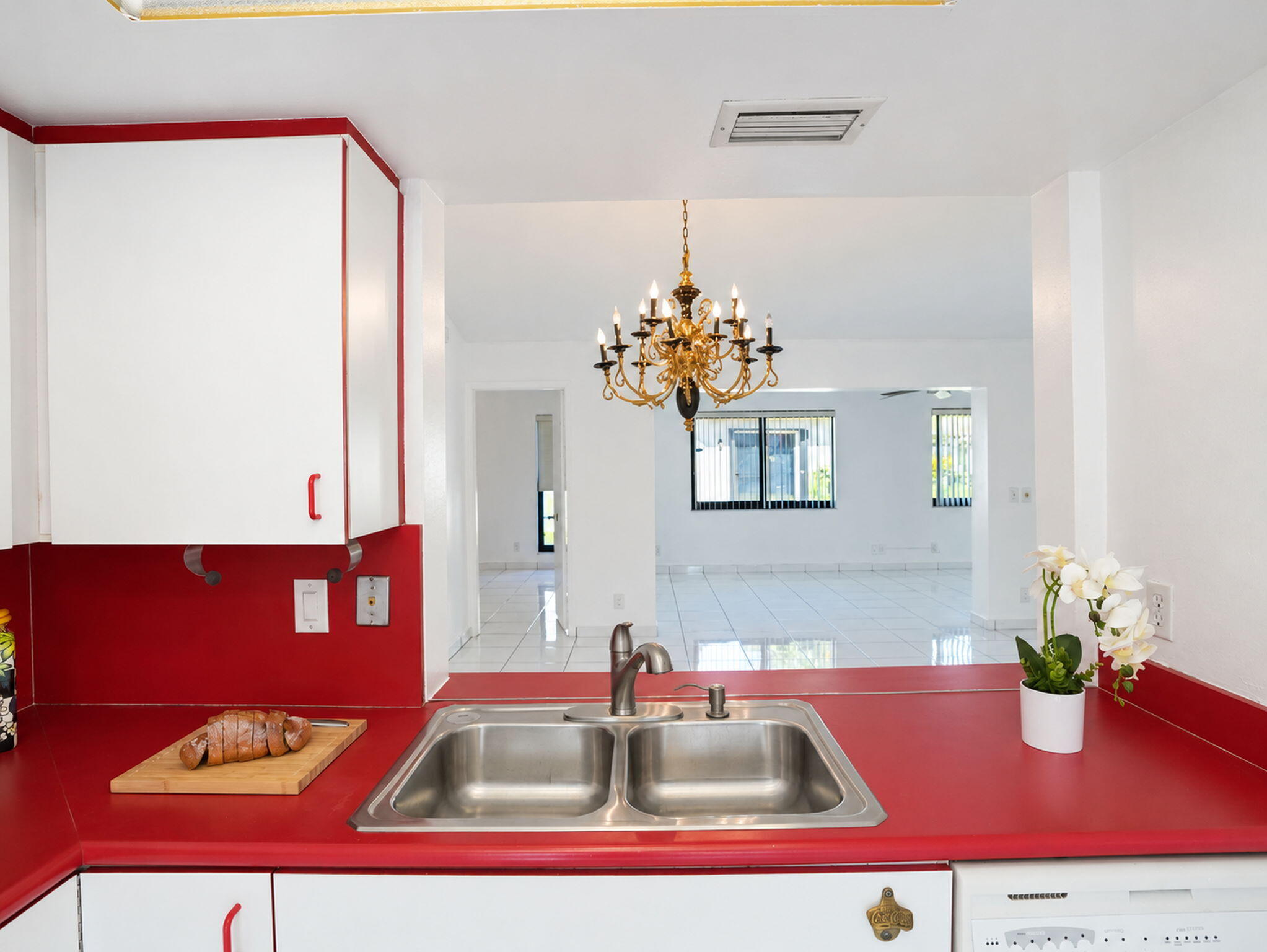 Kitchen featuring a dual-basin stainless steel sink, solid-surface countertop, cabinetry with red accents, and a brass-finished multi-bulb chandelier